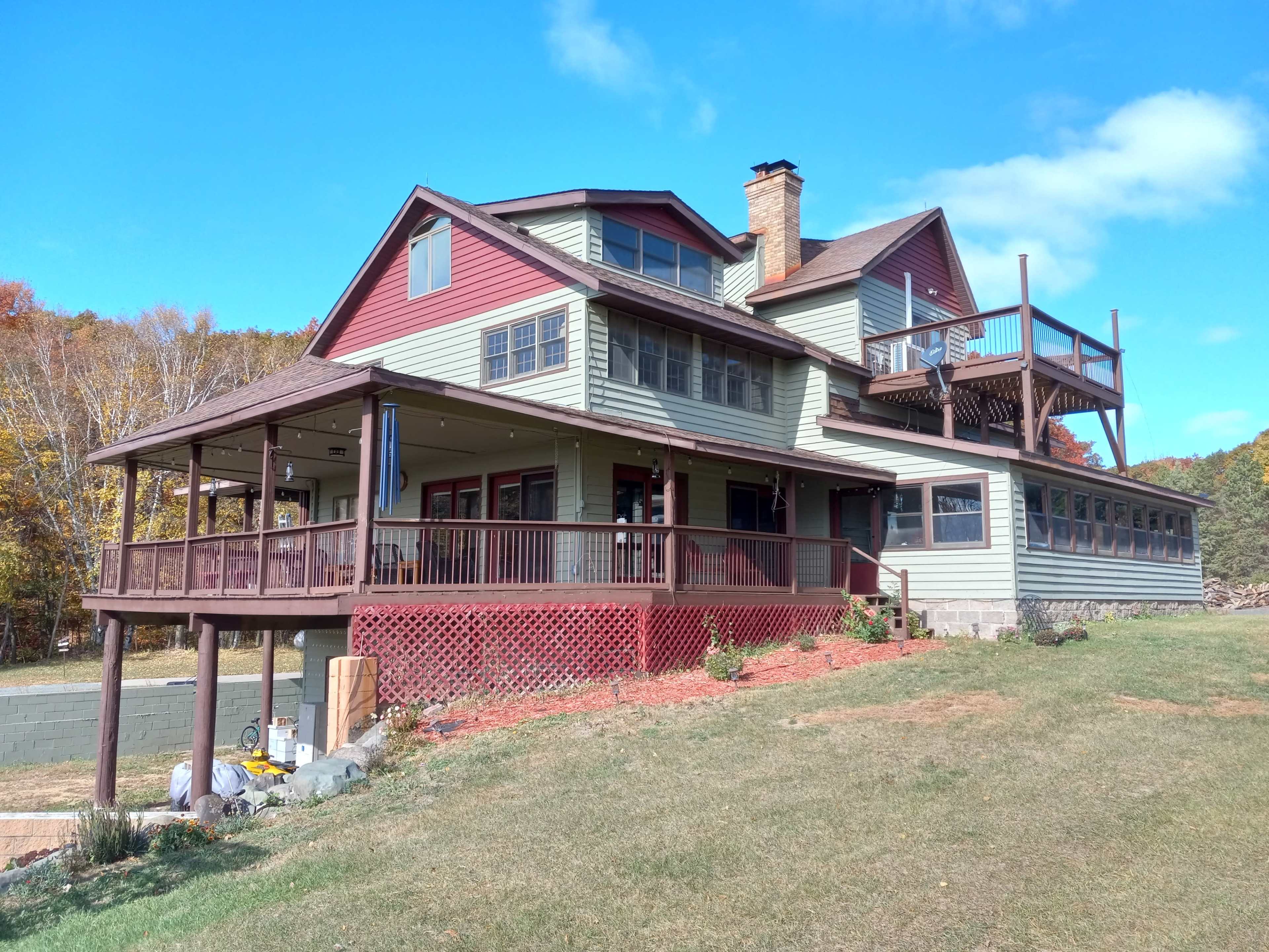 A two-story house with a mix of green and red siding, featuring multiple decks and a sloped lawn.