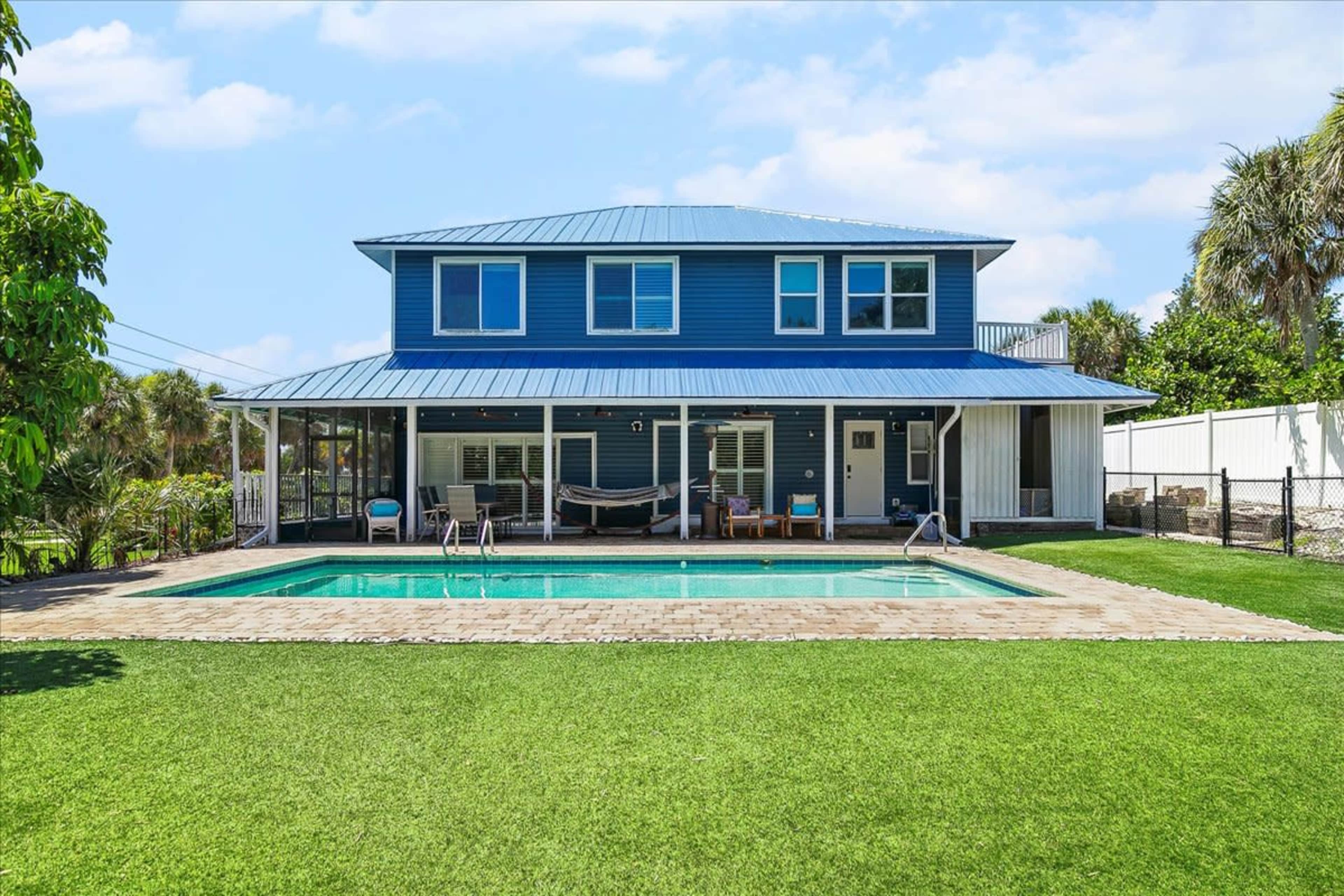 A two-story blue house with a metal roof features a swimming pool and a spacious backyard surrounded by greenery.