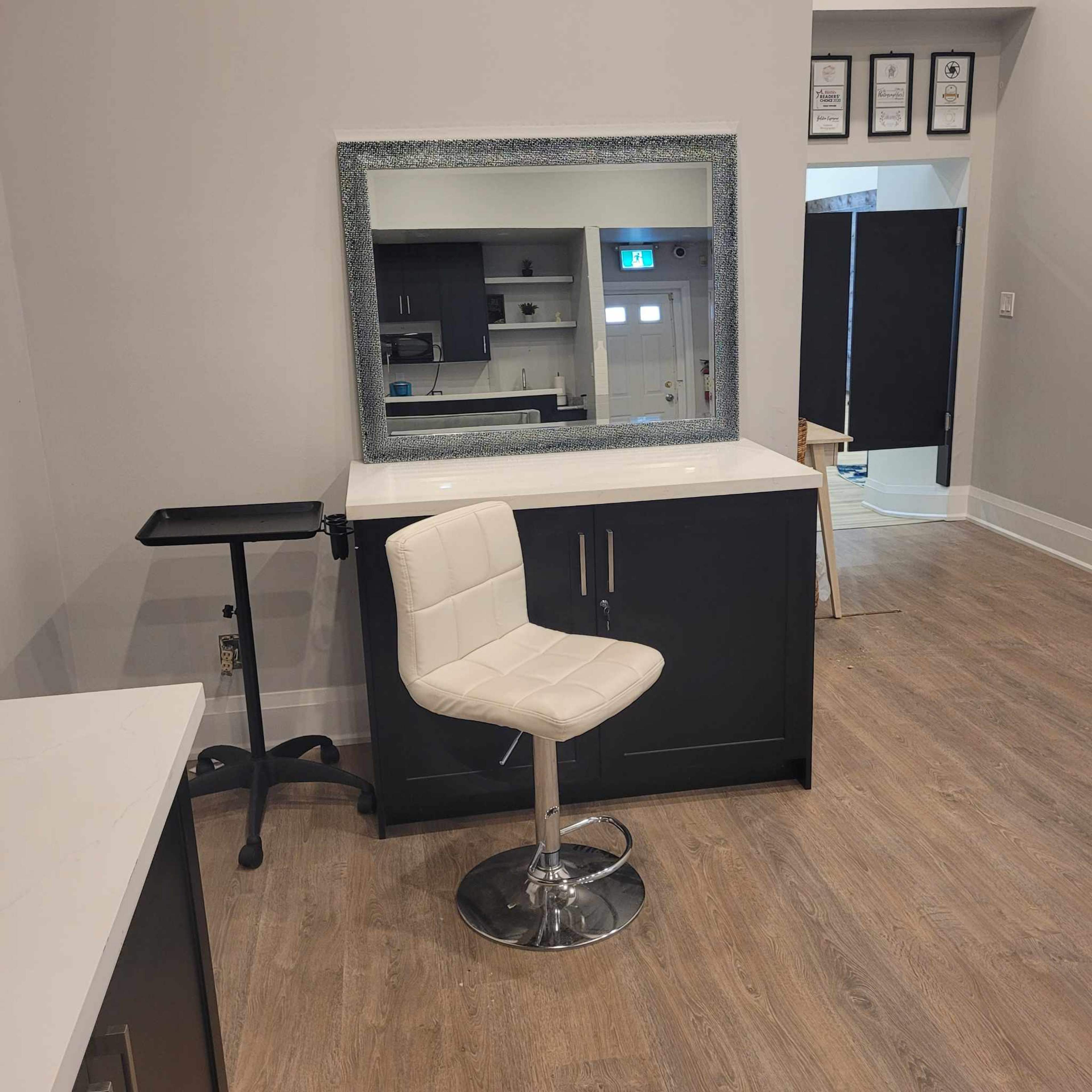 A modern interior space featuring a white bar stool in front of a large mirror, with a dark cabinet and a small table nearby.
