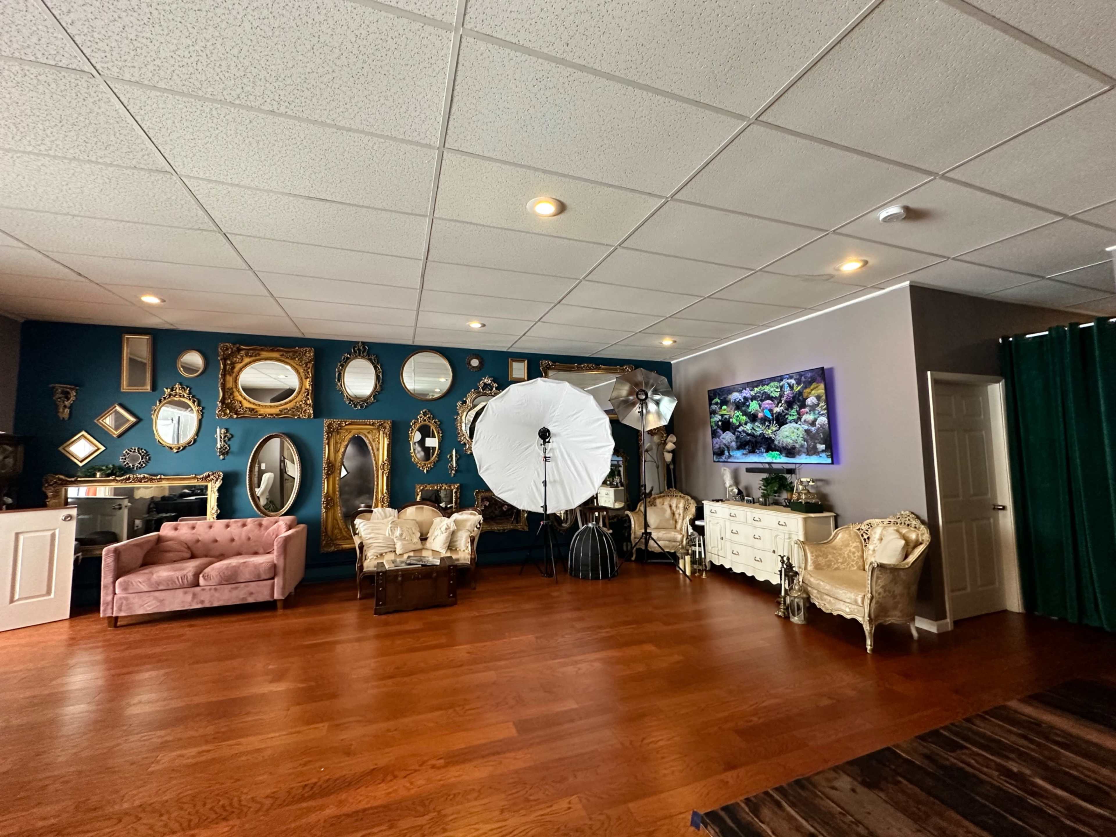 The scene shows a spacious room with a variety of mirrors arranged on one wall, a photography setup with a large softbox, and a mix of vintage and contemporary furniture.