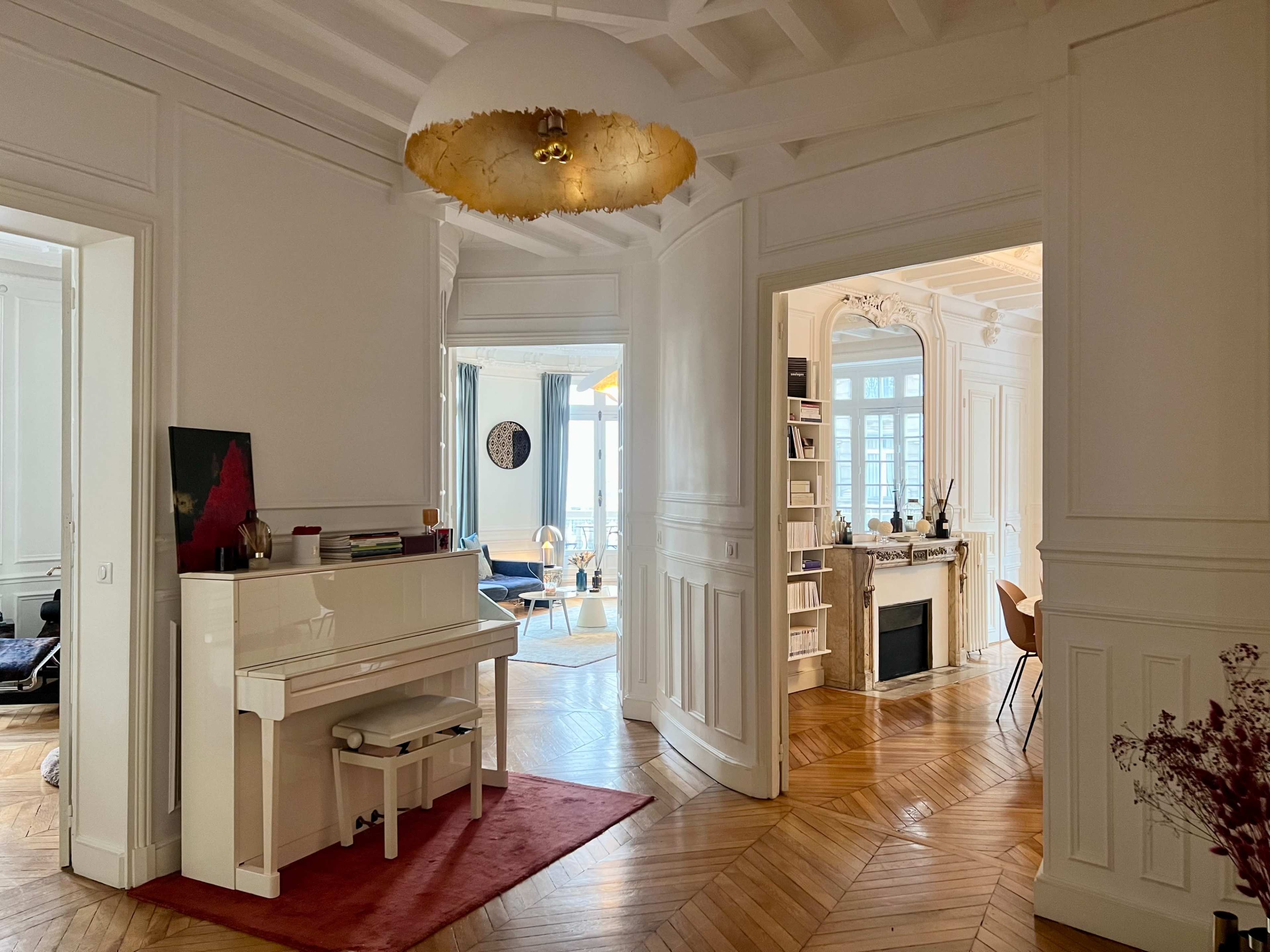 A bright interior of a home featuring a white piano, hardwood flooring, and an open layout leading to a living area.