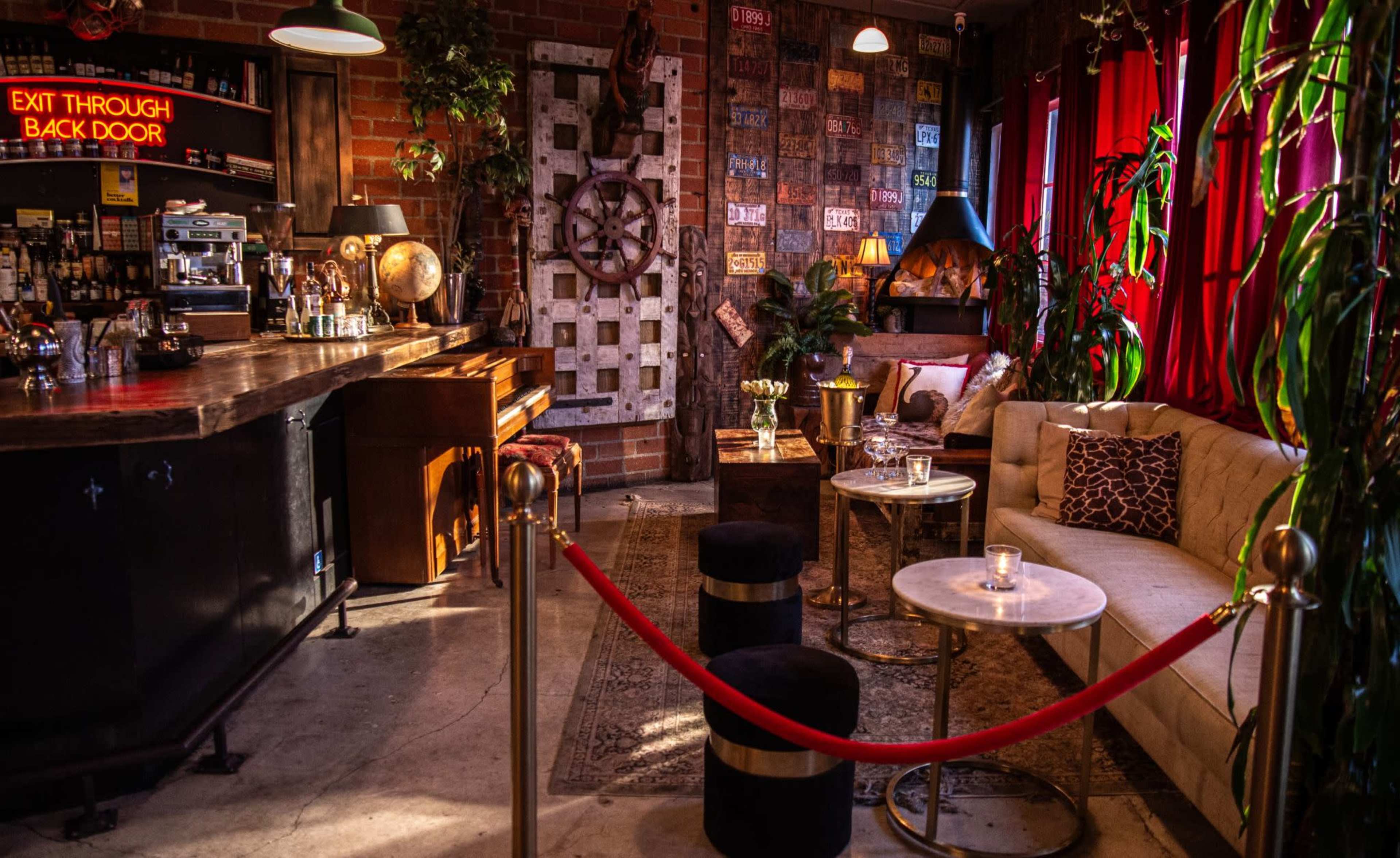 The image shows a cozy, well-decorated bar area with a piano, seating arrangements, and a vibrant color palette created by red curtains and various decor items.