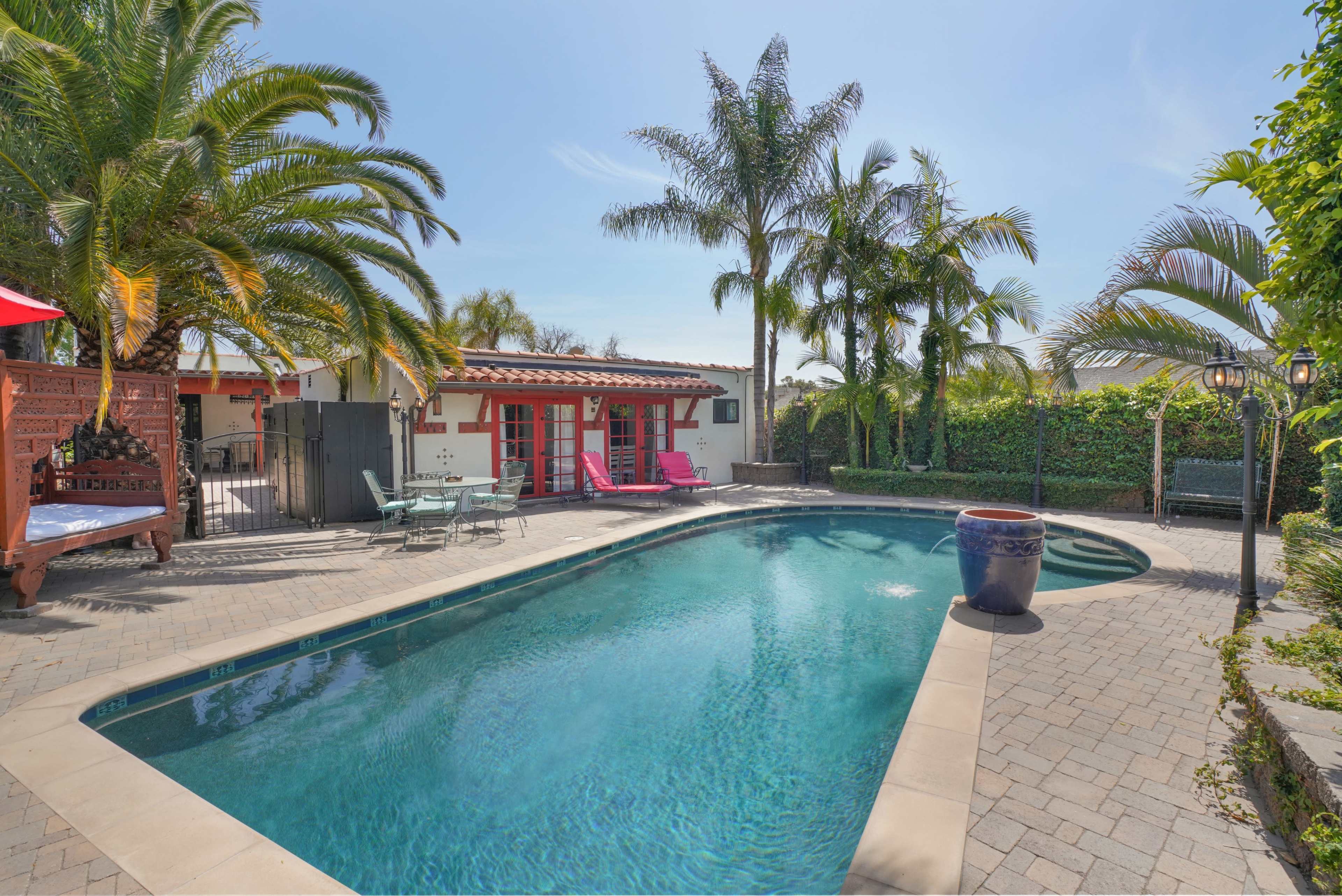 A swimming pool surrounded by palm trees and outdoor seating in a sunlit backyard.