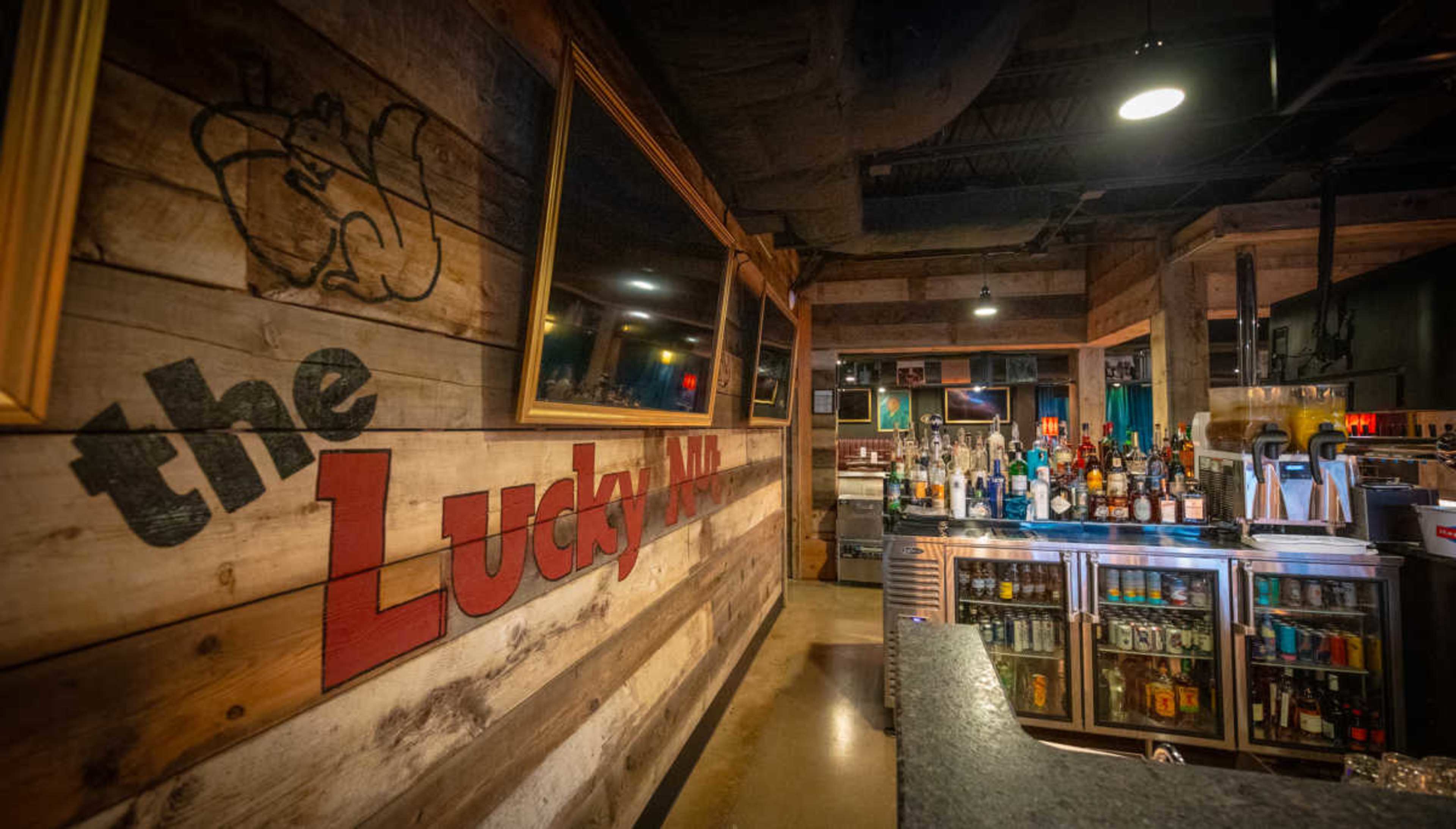 The image features a wooden bar interior with a prominent sign reading "the Lucky" and a well-stocked bar displaying various bottles of alcohol.