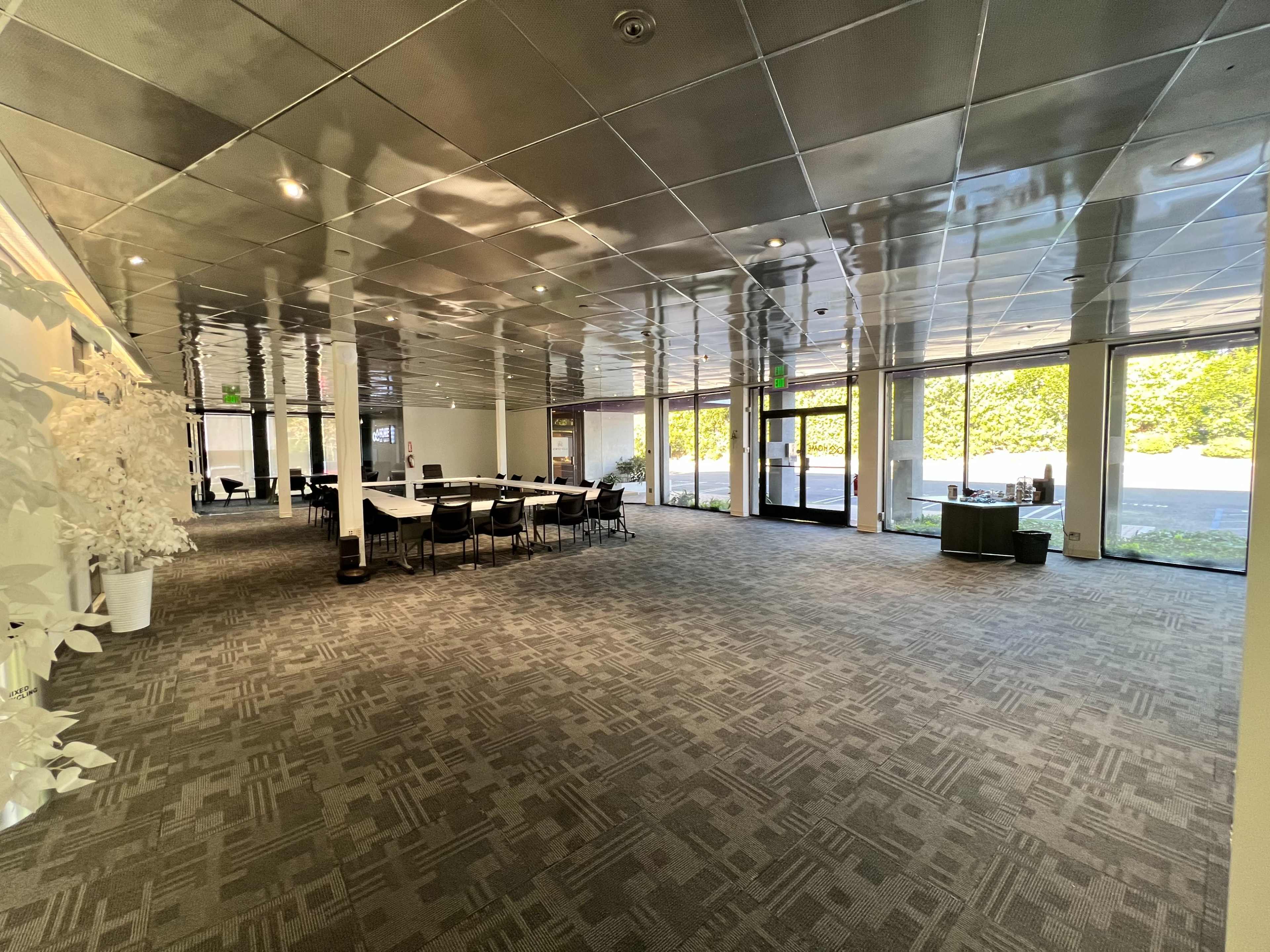 A modern, spacious interior of a building with a seating area arranged around a central table and large windows providing natural light.