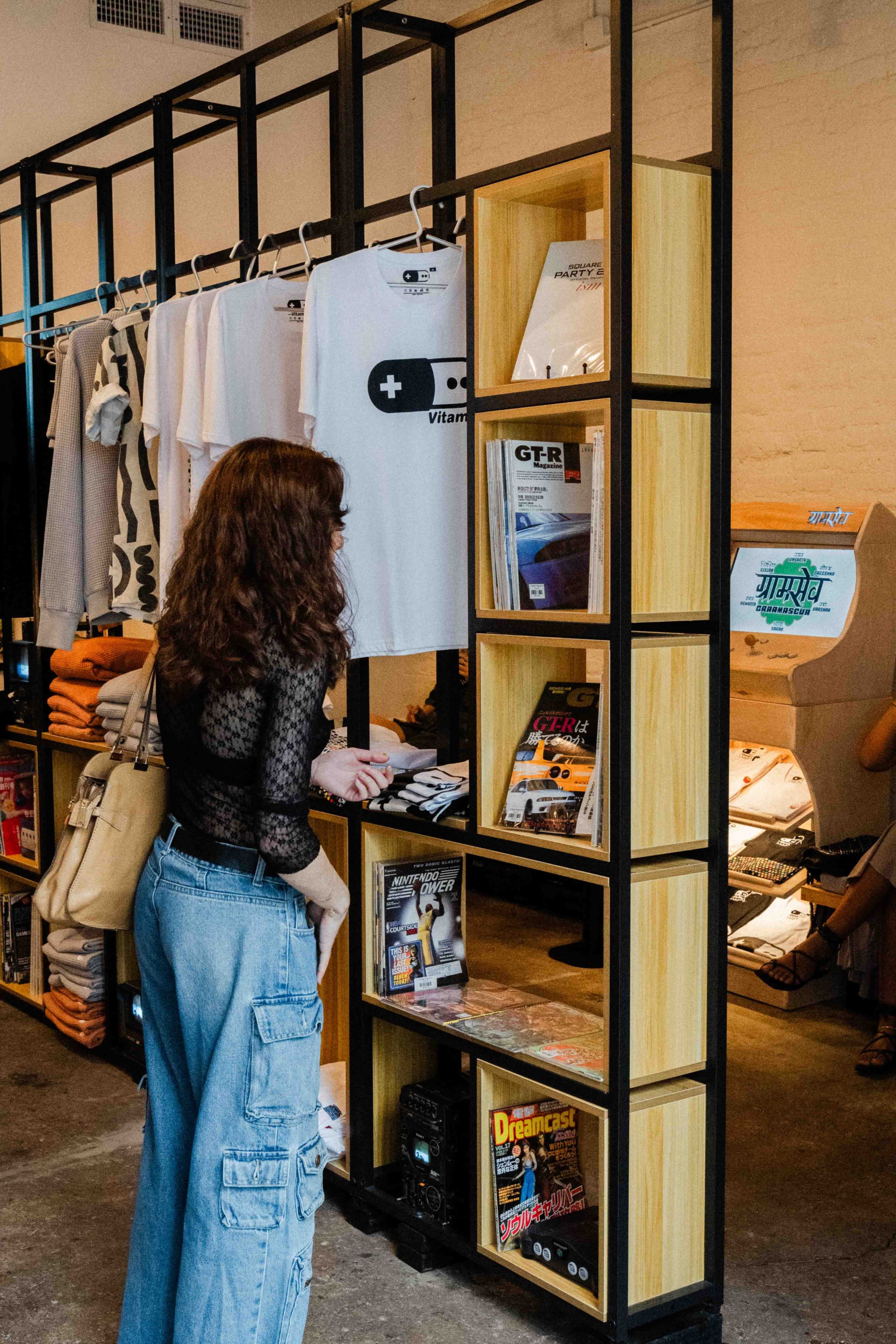 A woman browses a display of clothing and magazines in a retail space.