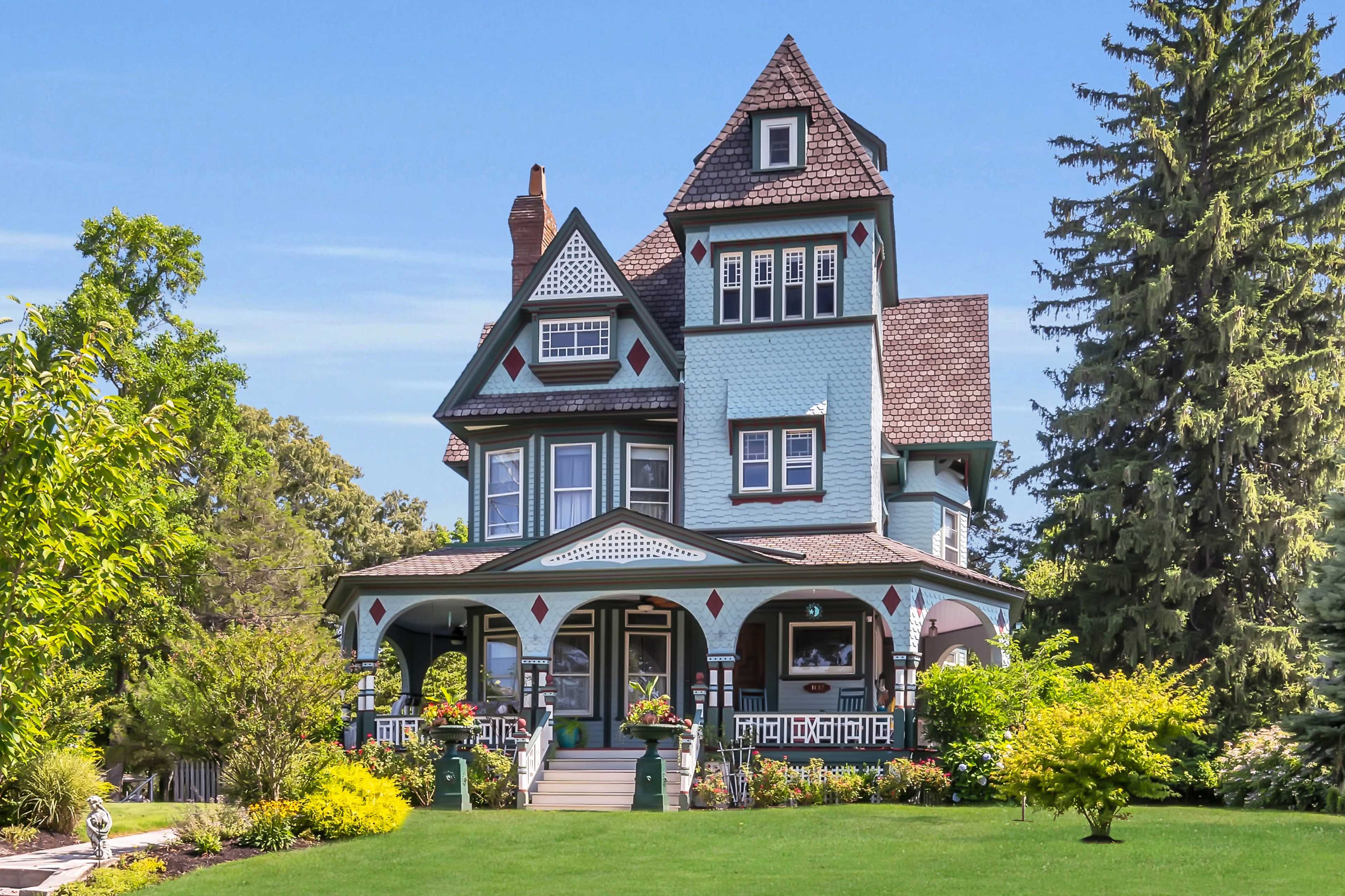 A large, colorful Victorian-style house with a prominent tower, surrounded by well-maintained gardens and trees.