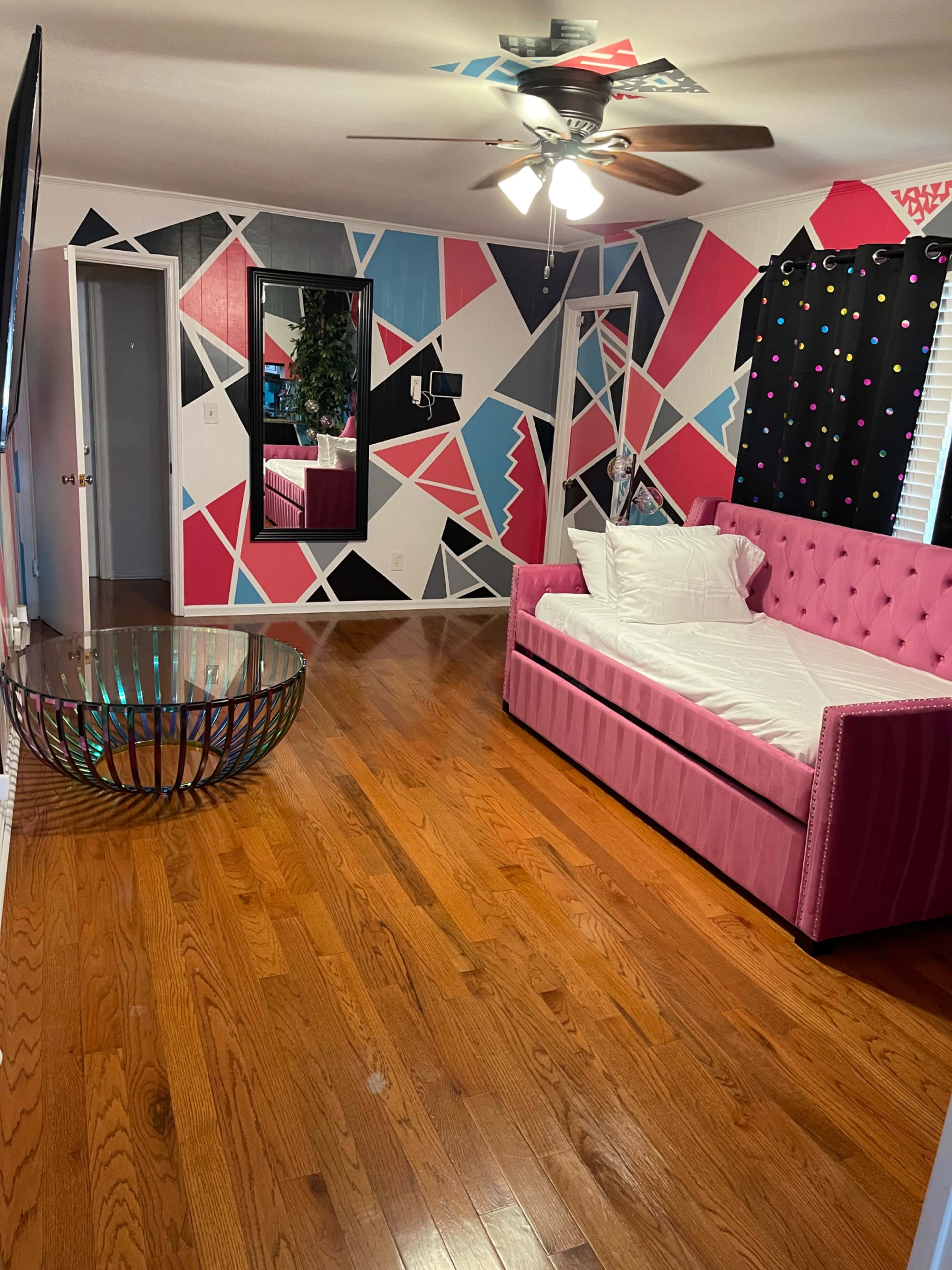 A room with a pink upholstered couch, a modern metallic coffee table, and a wall featuring a geometric, multicolored design.