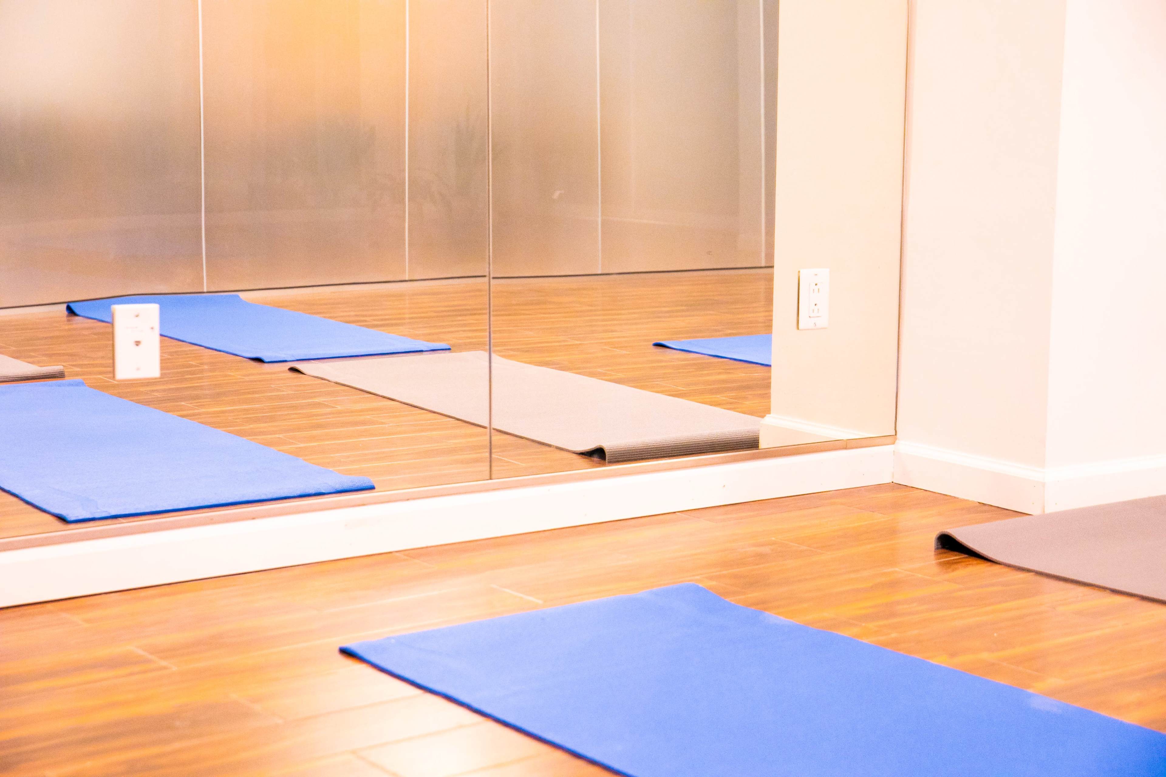 Several yoga mats arranged on a wooden floor in front of a mirrored wall.