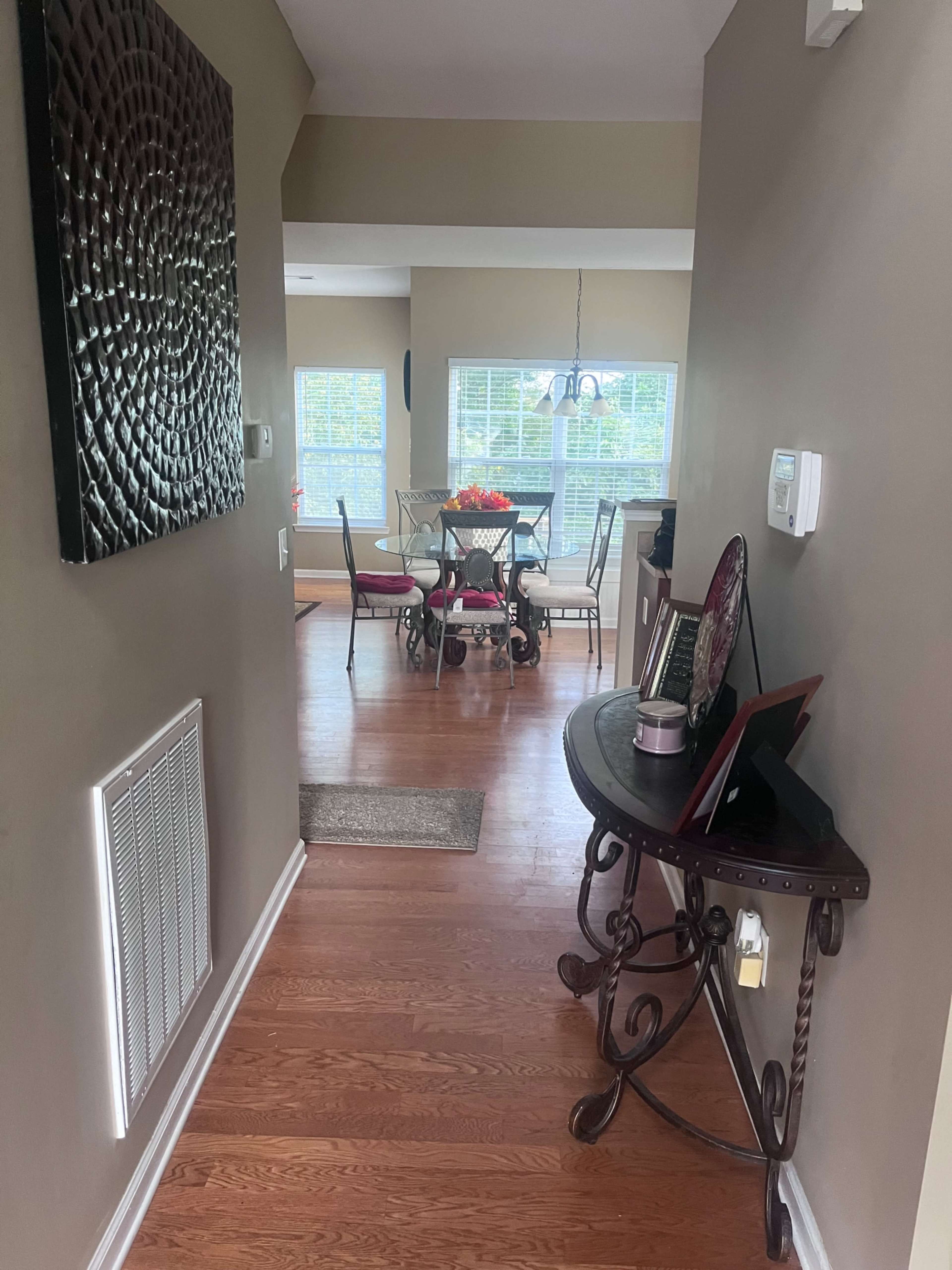 A hallway leads to a dining area with a table set for four and large windows letting in natural light.
