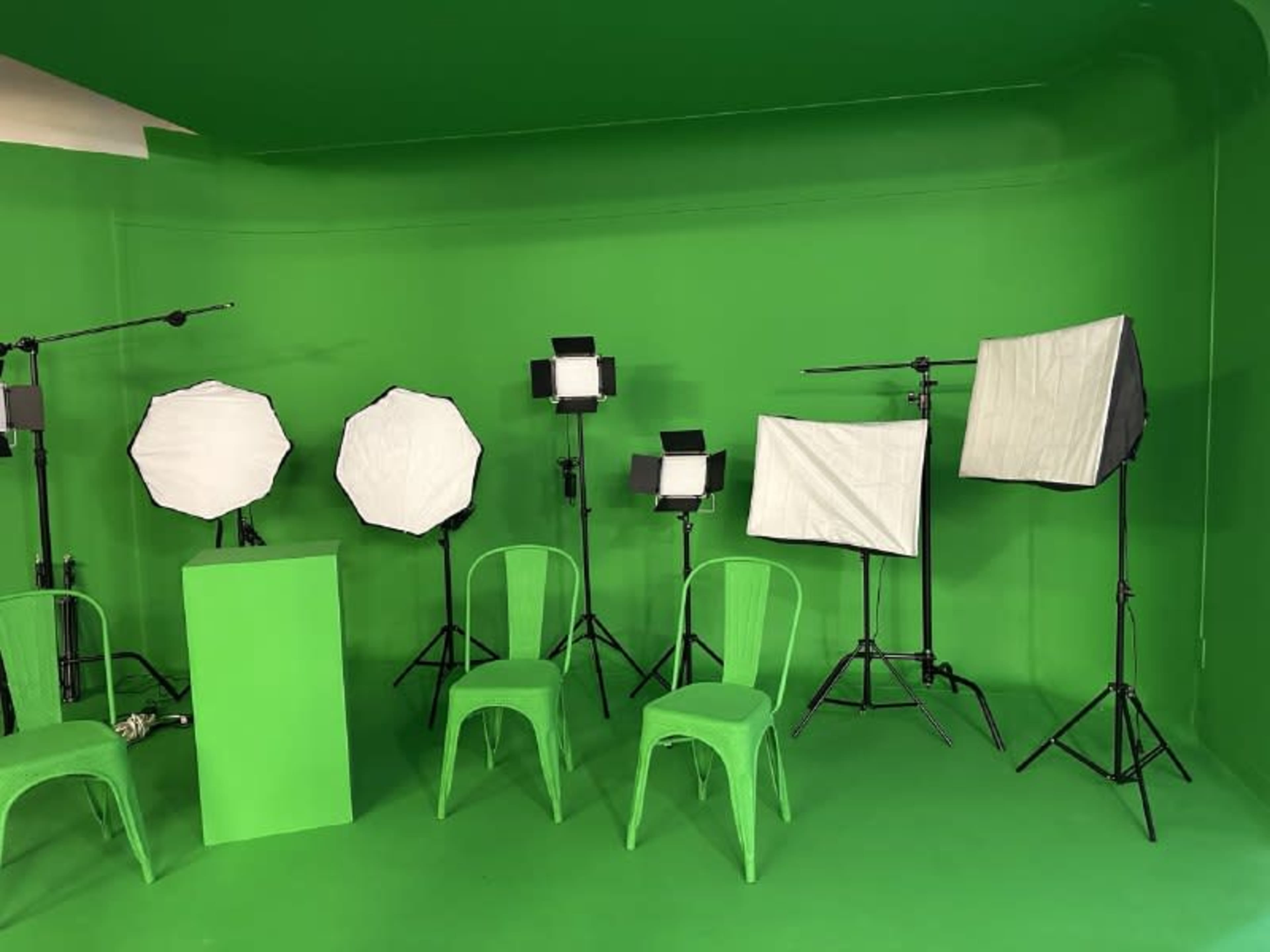 The image shows a green studio setup with two chairs, a pedestal, and multiple lighting equipment arranged against a green backdrop.