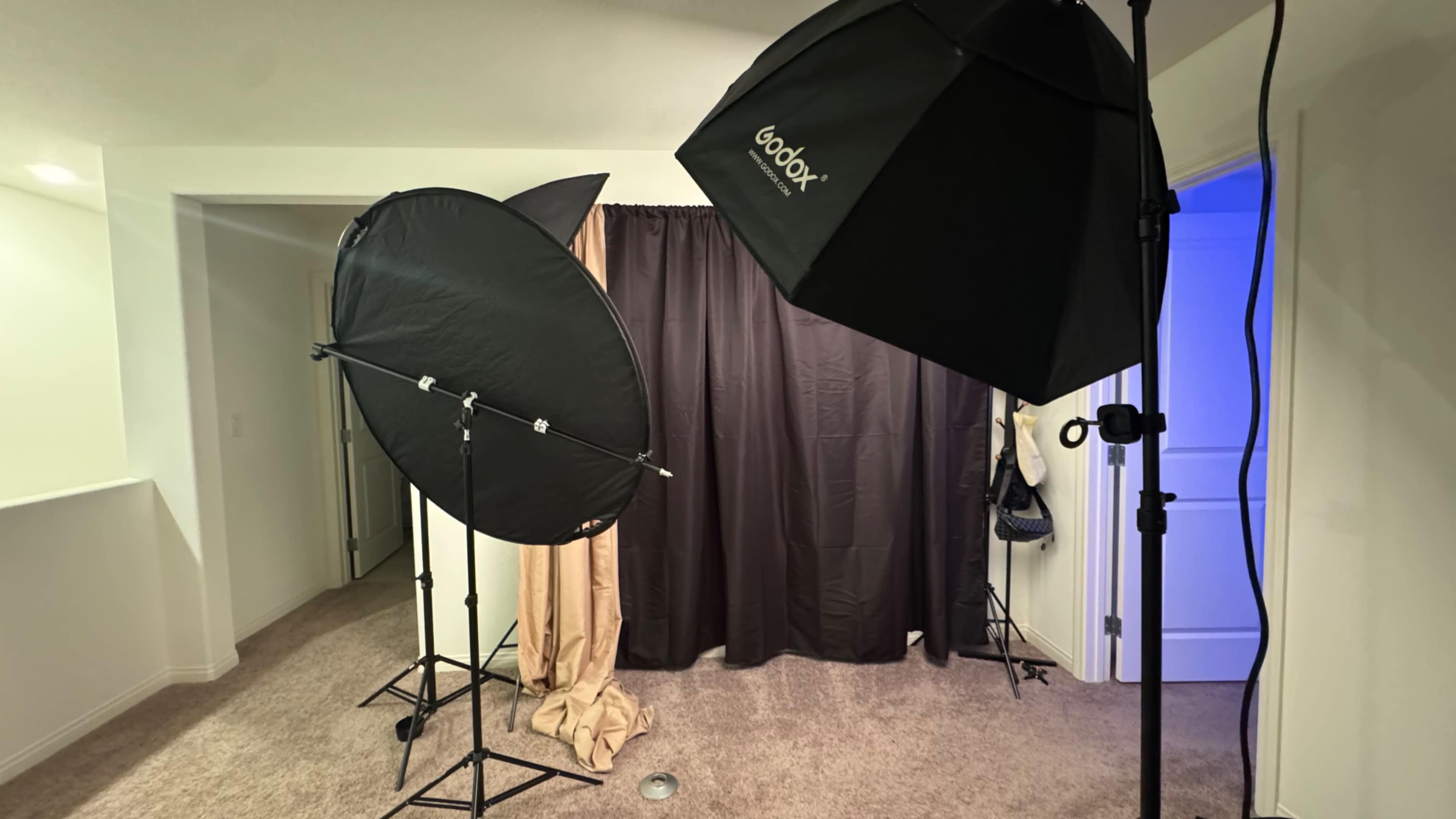 The image shows a photography setup featuring two softbox lights facing a black curtain in a room with carpeted flooring.