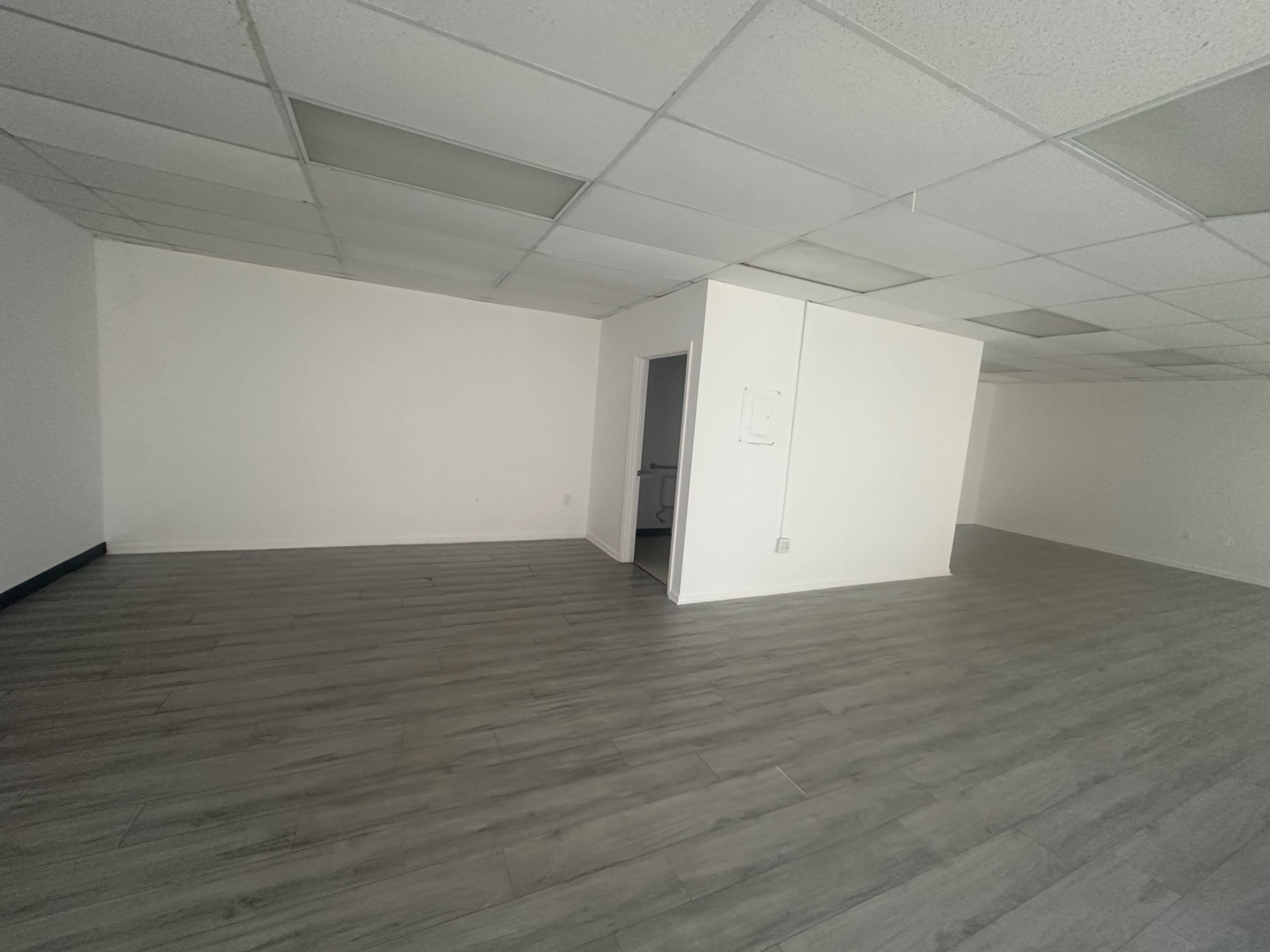 The image shows a vacant room with gray flooring and white walls, featuring a small doorway leading to another space.