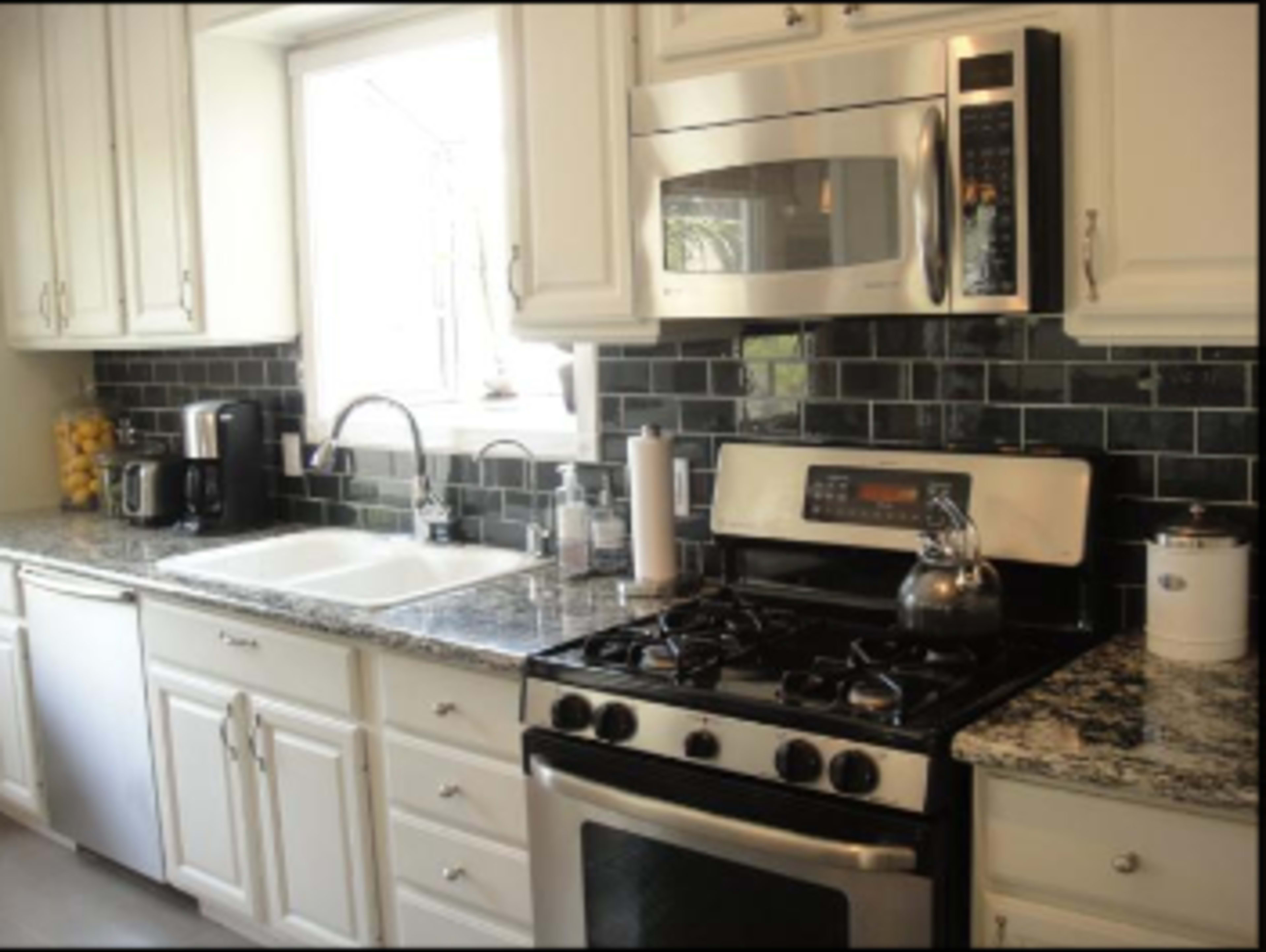 The kitchen features stainless steel appliances, a double sink, and dark tiled backsplash with a granite countertop.