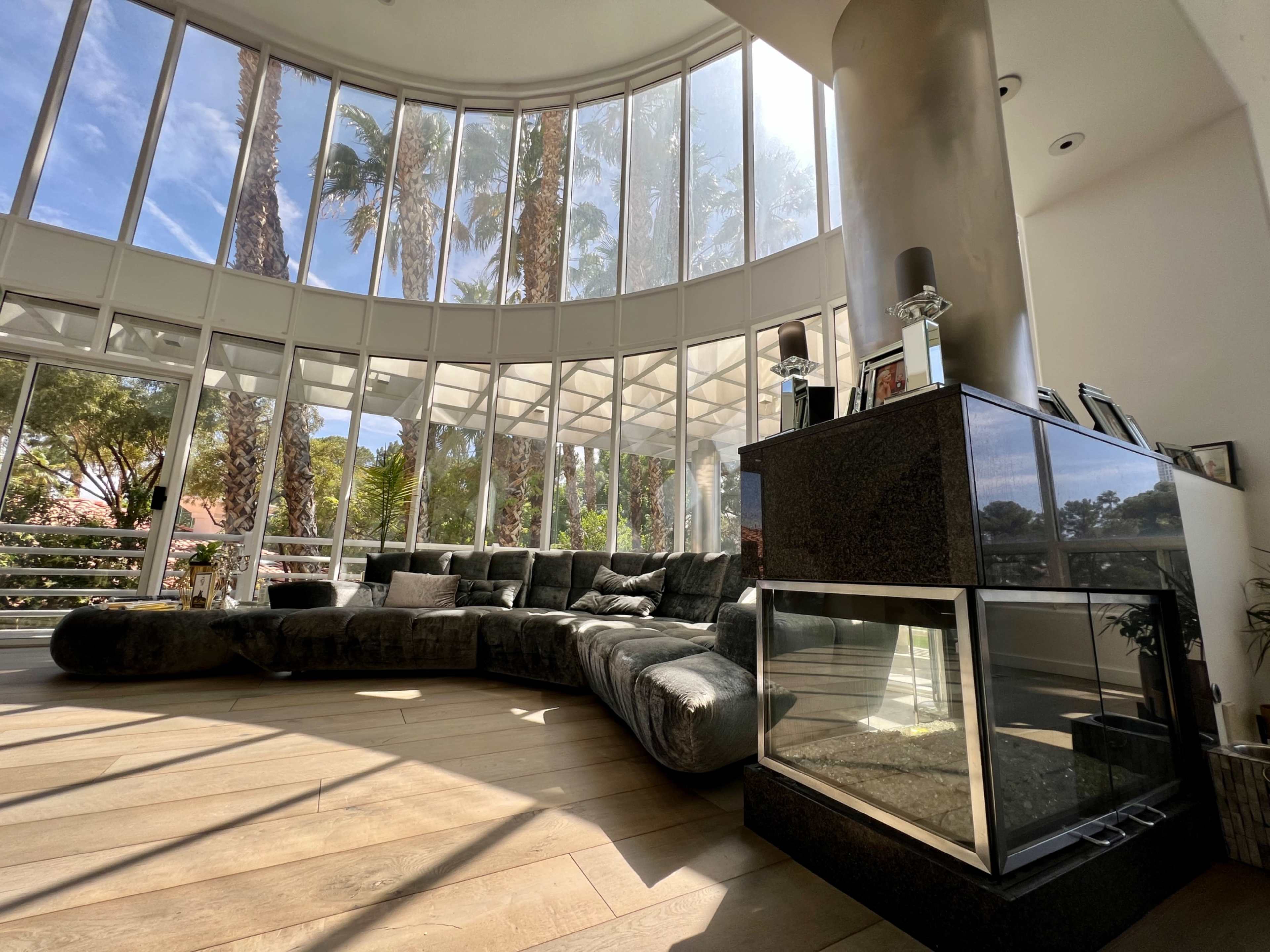 A spacious living room features a curved sofa and large windows with views of palm trees.