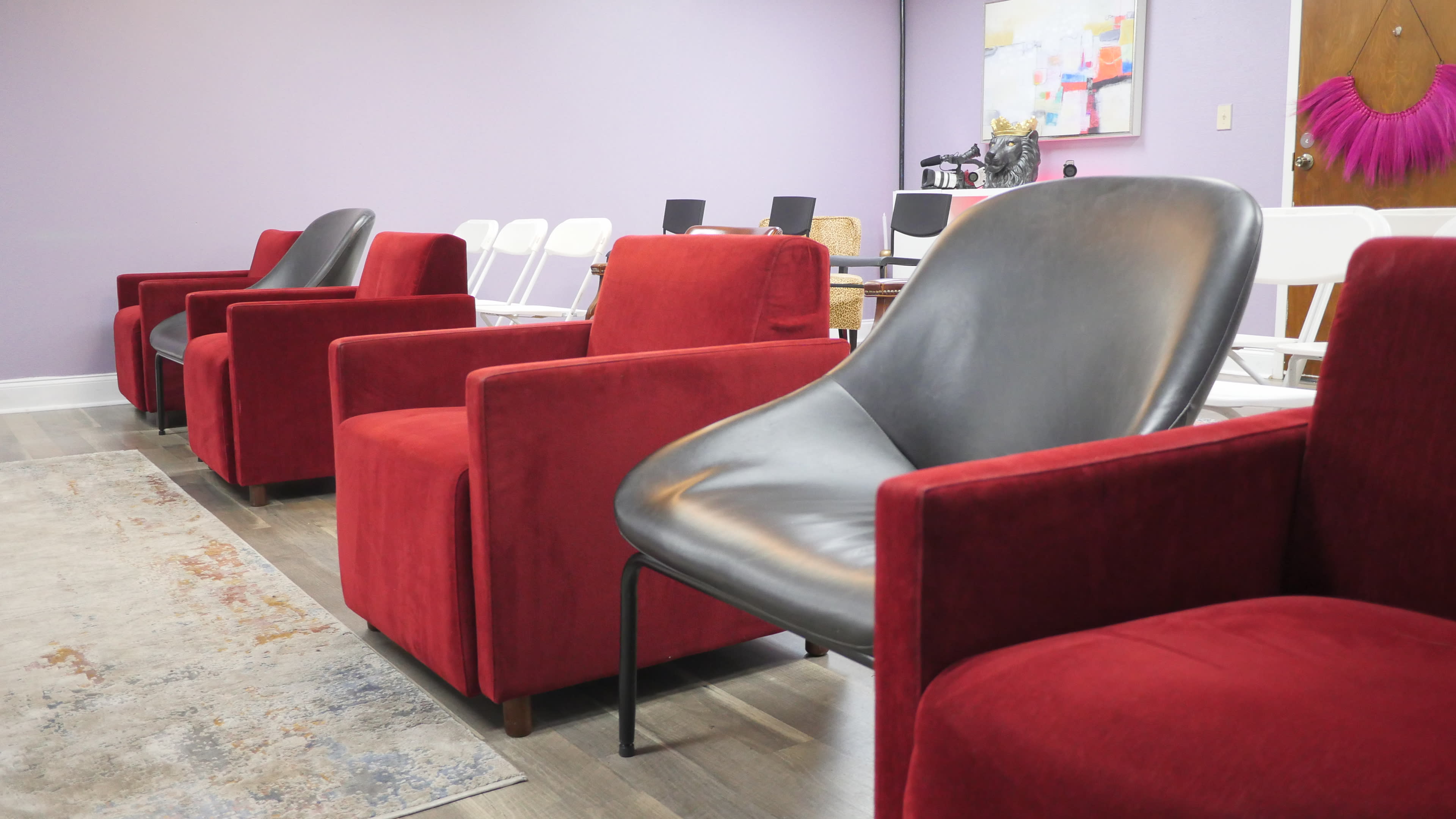 A row of red and black chairs in a room with purple walls and various furniture in the background.