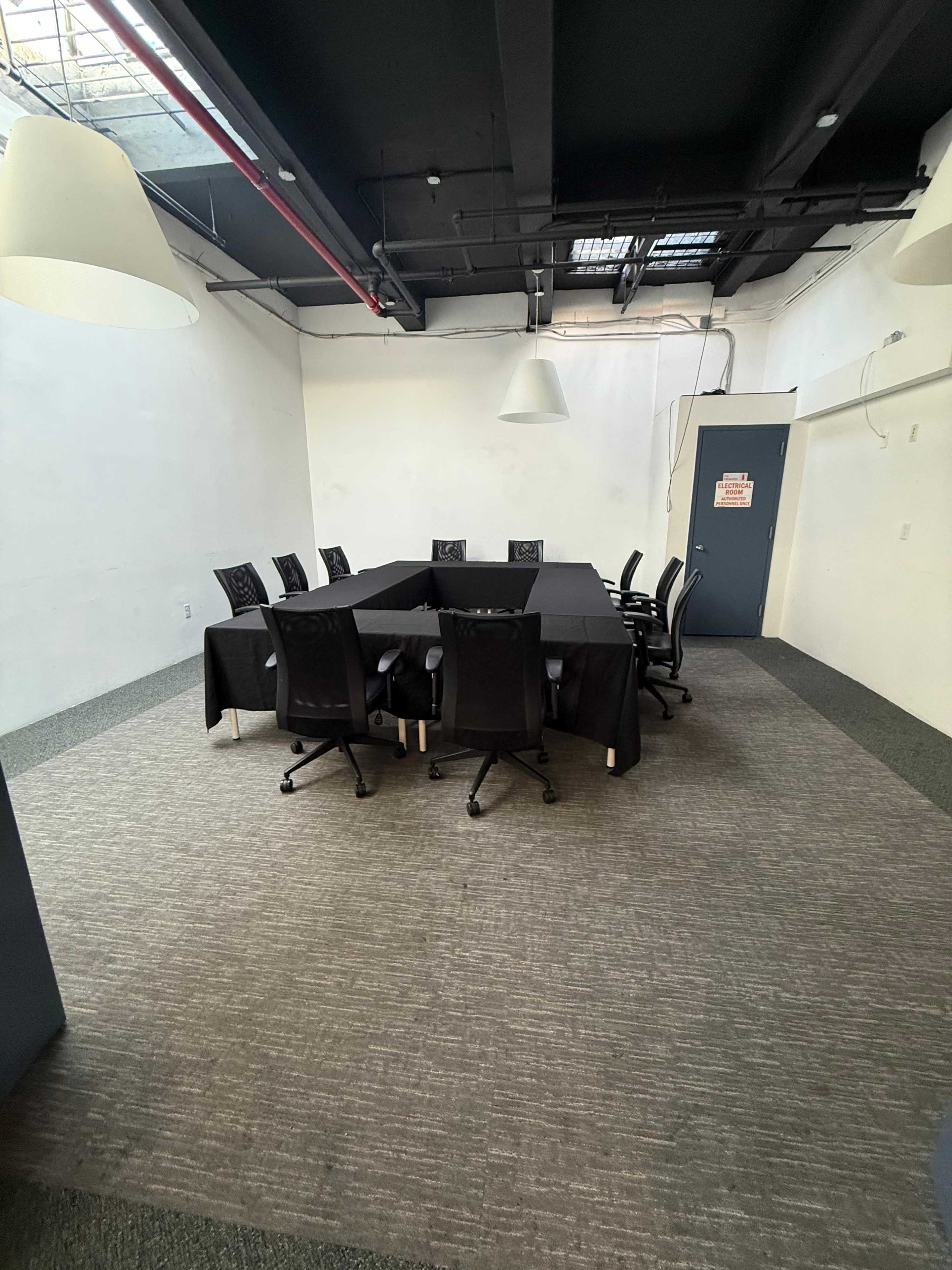 The image shows a large conference room with a rectangular table surrounded by black office chairs and minimal decor.