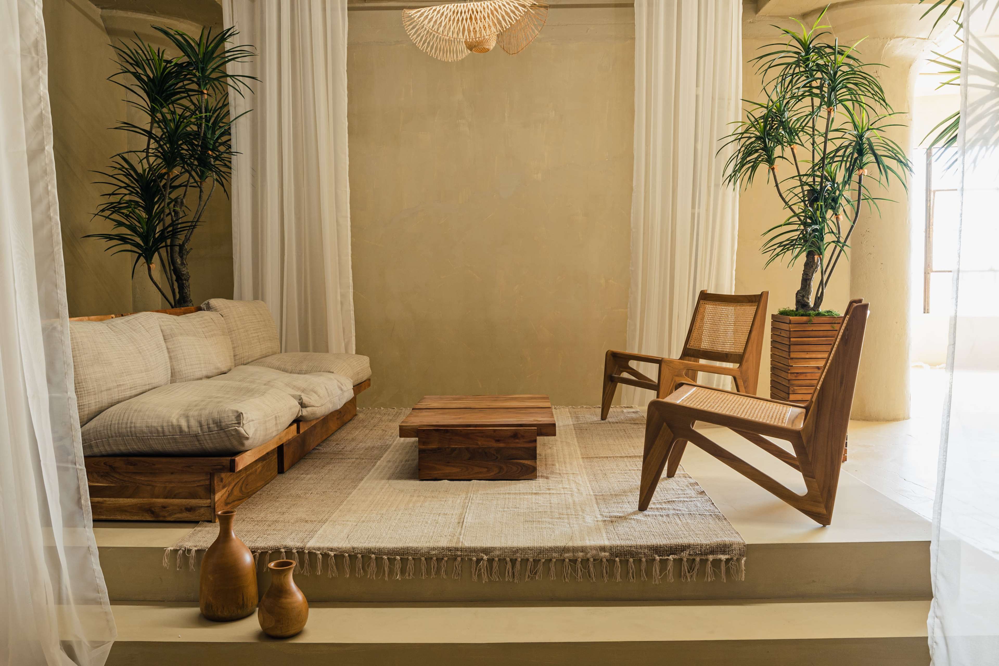 A minimalist living space featuring a wooden coffee table, a sectional sofa, and two chairs, accompanied by potted plants and decorative vases.