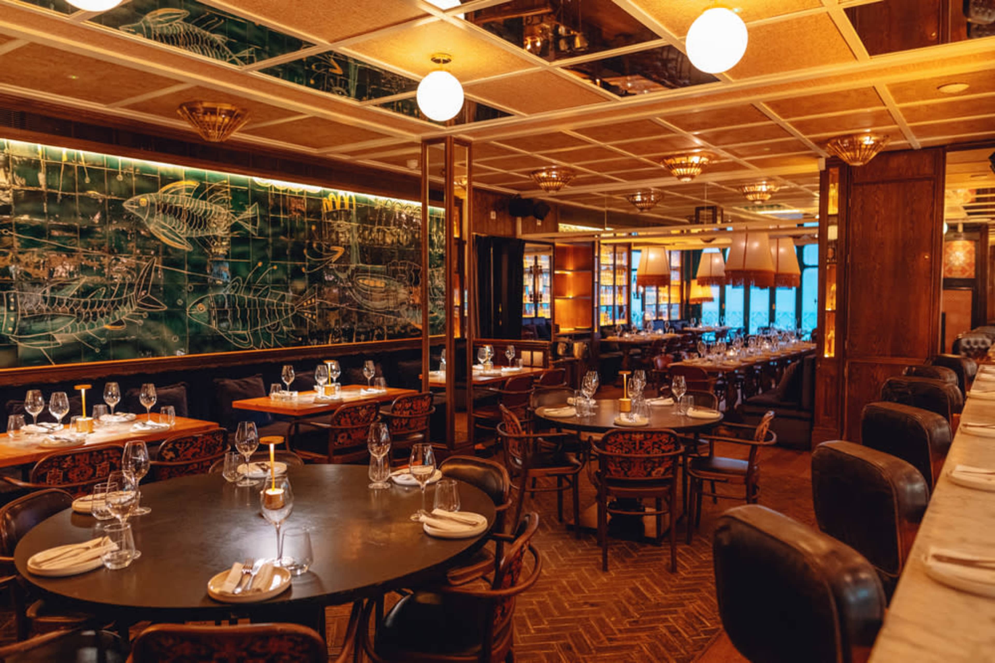 An elegantly designed restaurant interior with circular tables set for dining and a large green mural depicting fish on the wall.