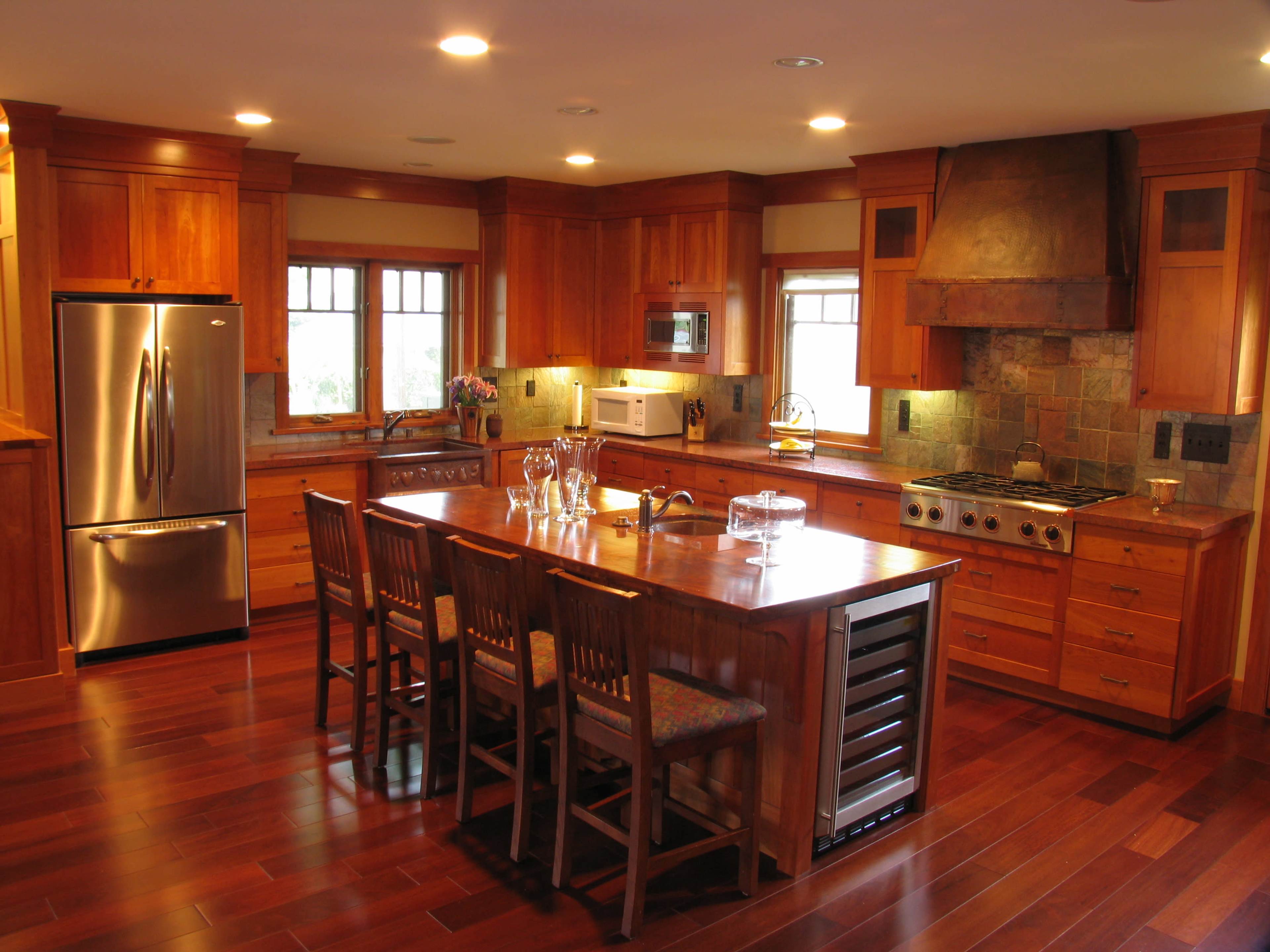 The kitchen features wooden cabinetry, a central island with seating for six, stainless steel appliances, and a stone backsplash.