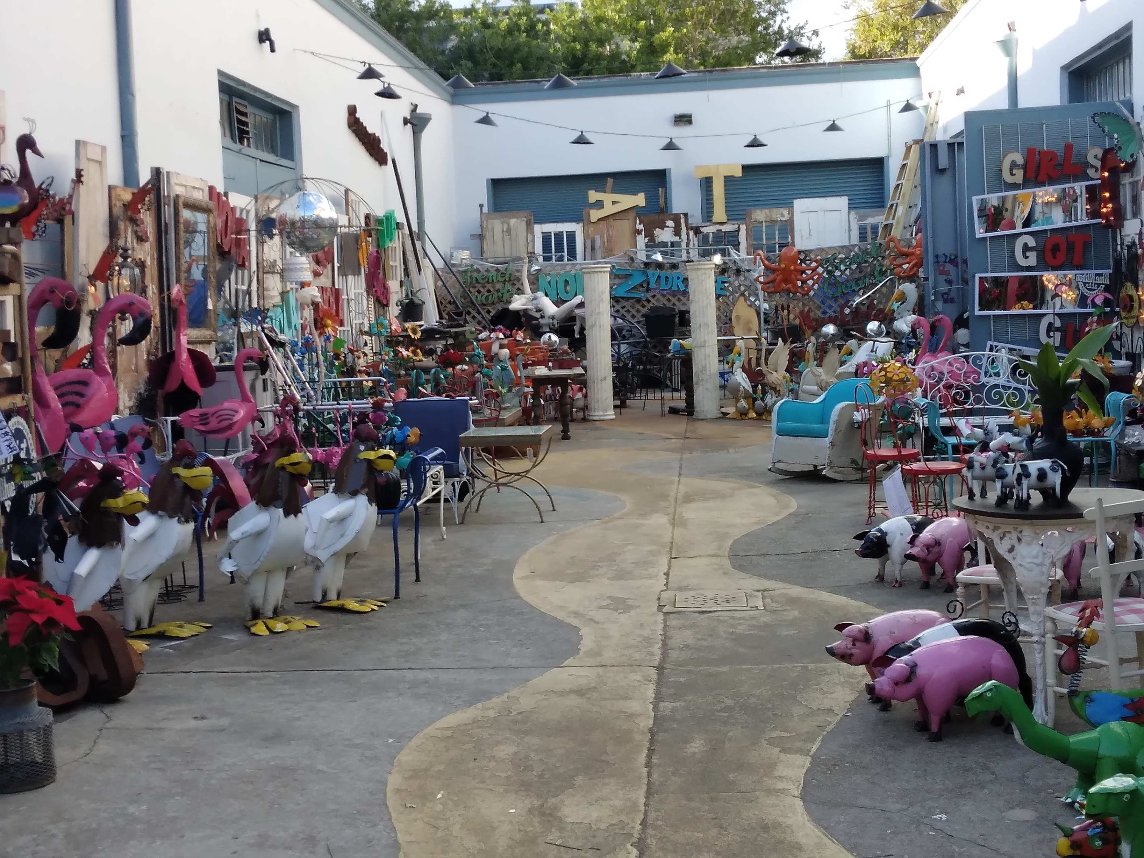 The image shows an outdoor courtyard filled with various colorful decorations, including flamingos, swans, and whimsical furniture.