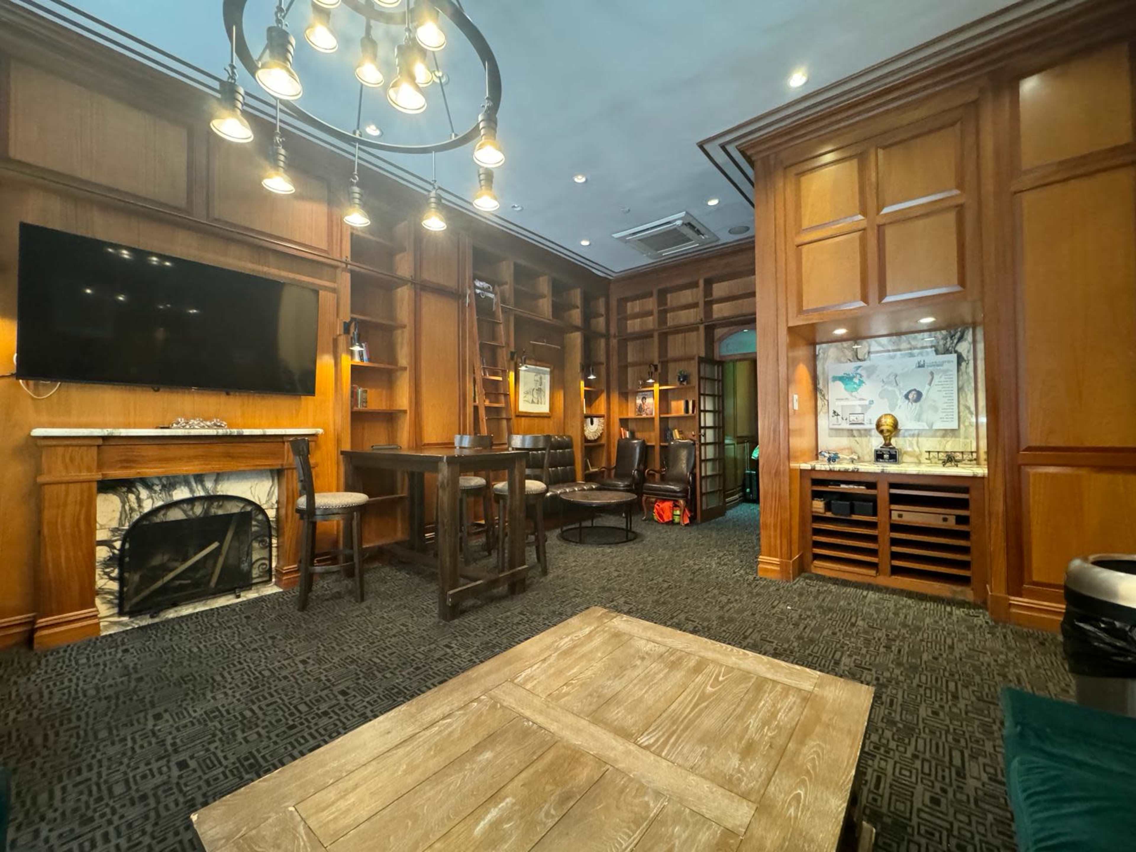 A cozy, wood-paneled room featuring a fireplace, a large television, a bar-style table, and shelves filled with books and decor.
