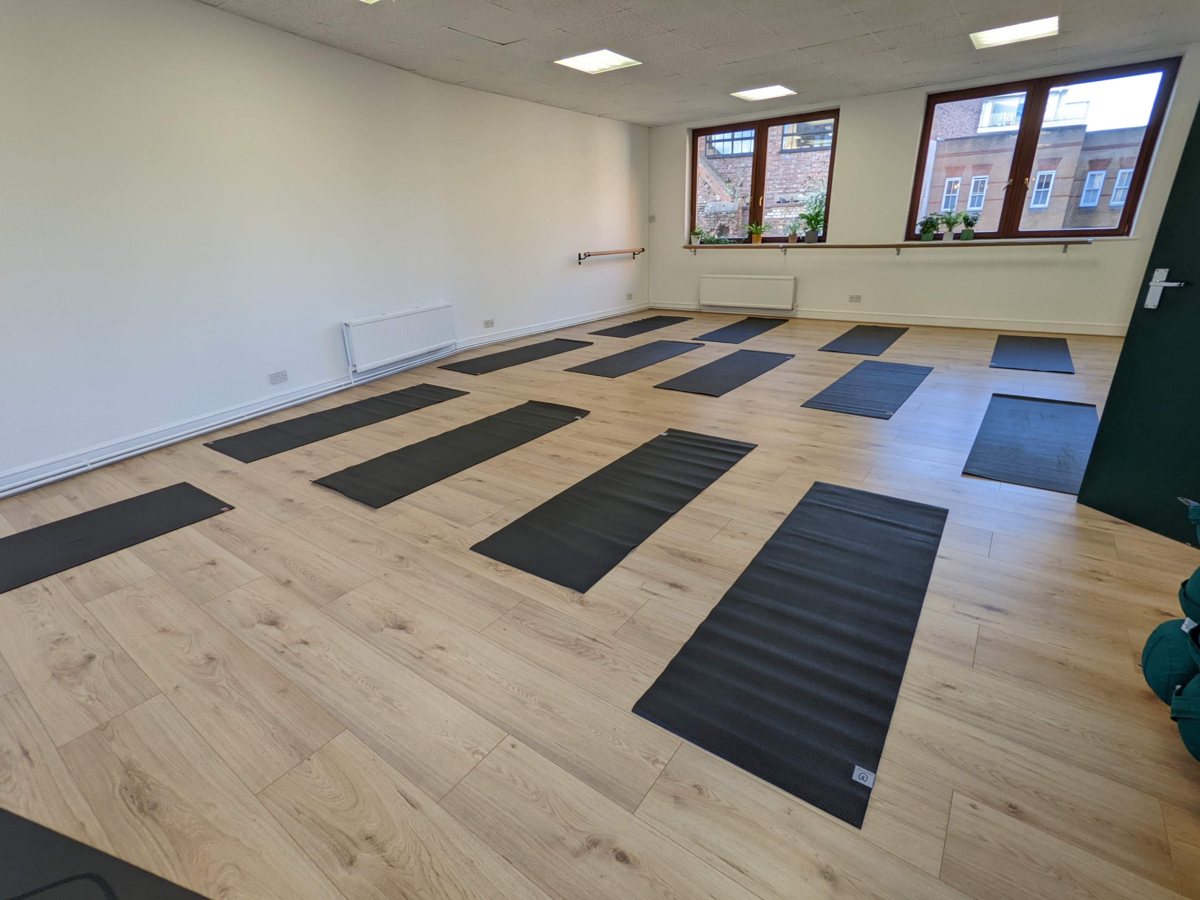 A spacious room with wooden flooring, featuring several yoga mats arranged neatly in rows.