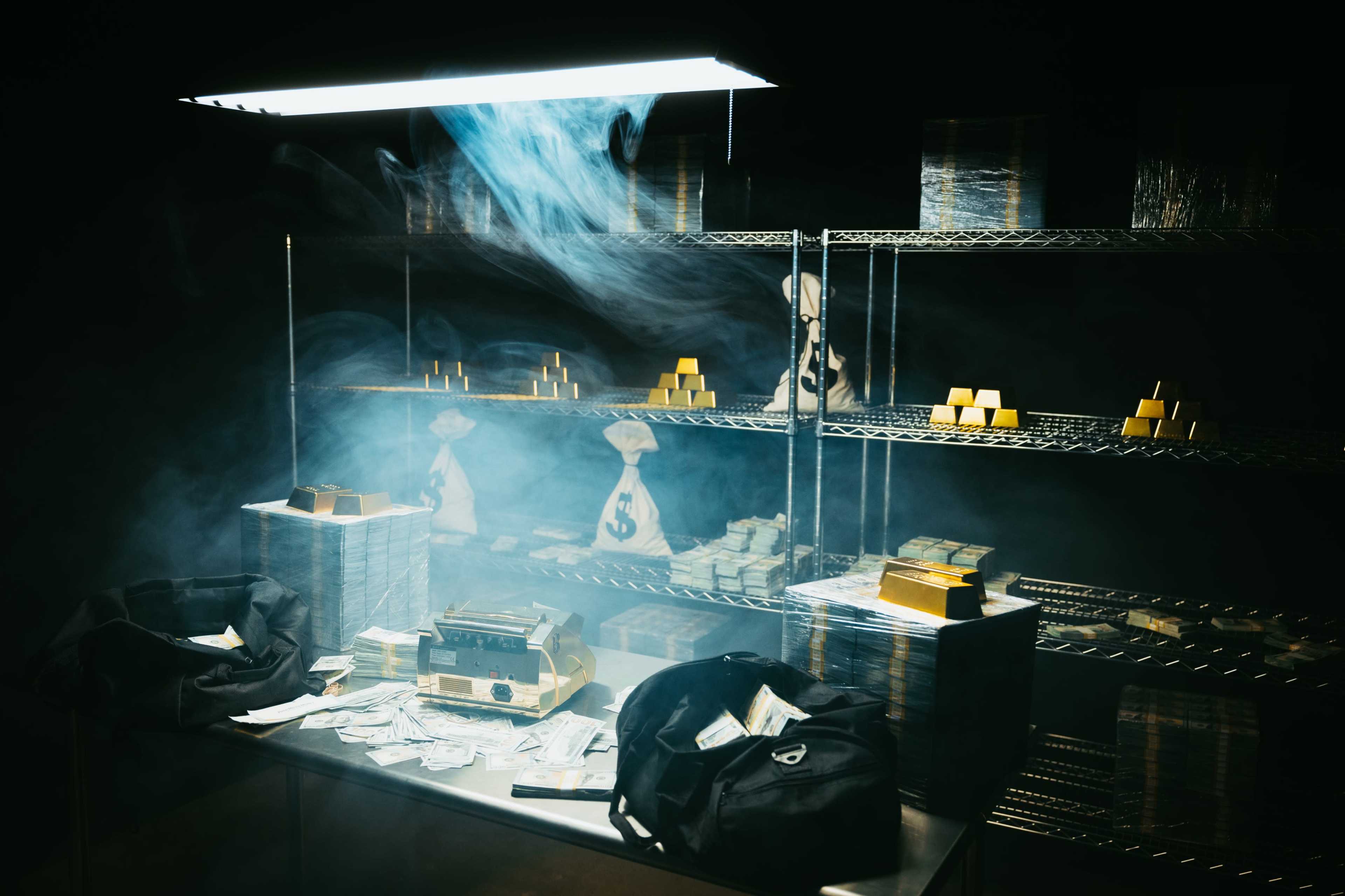 The image shows a dimly lit room filled with stacks of cash, gold bars on shelves, and two bags on a table.