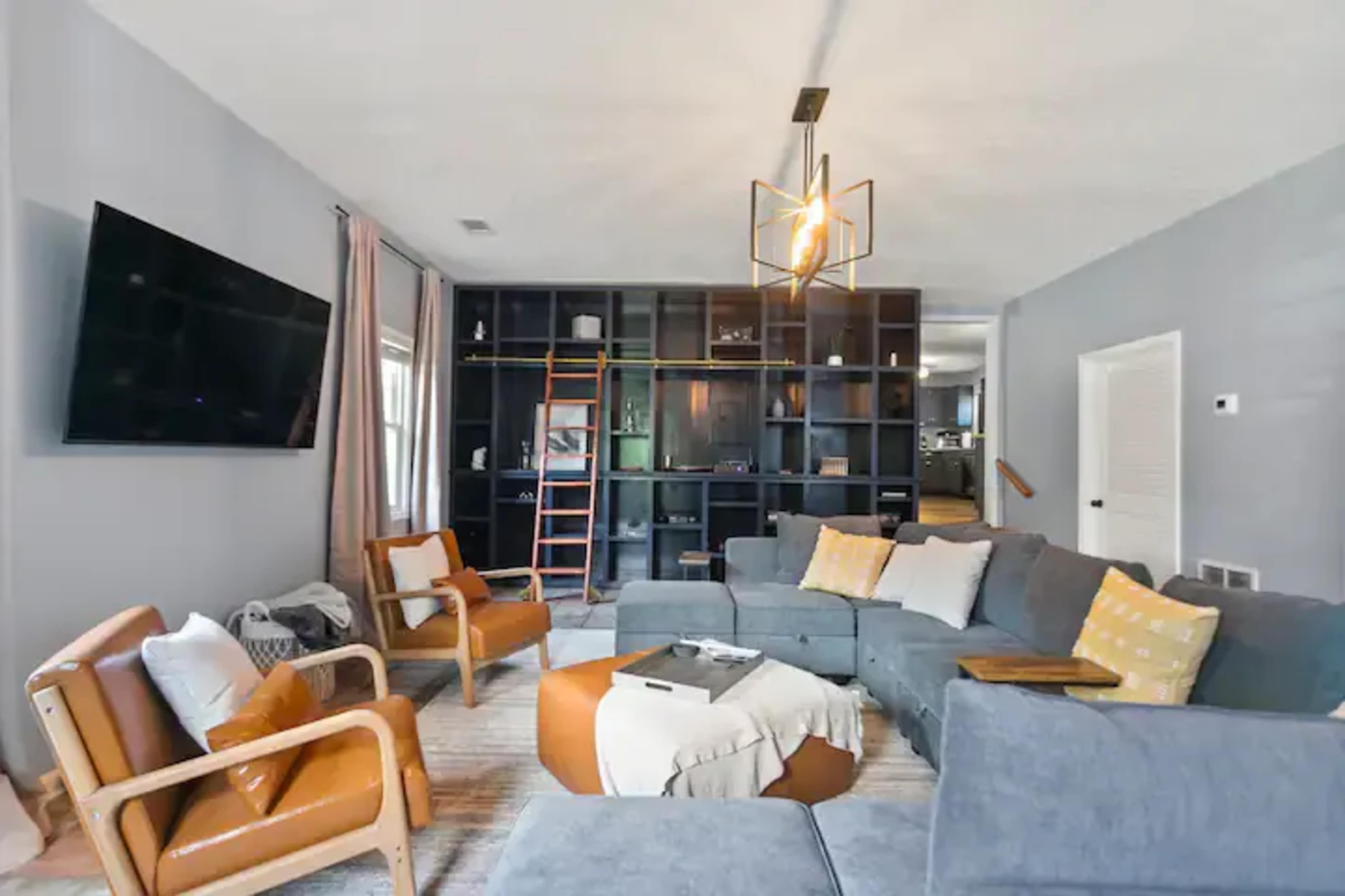 The living room features a sectional sofa, two armchairs, a coffee table, and a large wall-mounted television against a backdrop of built-in shelves.