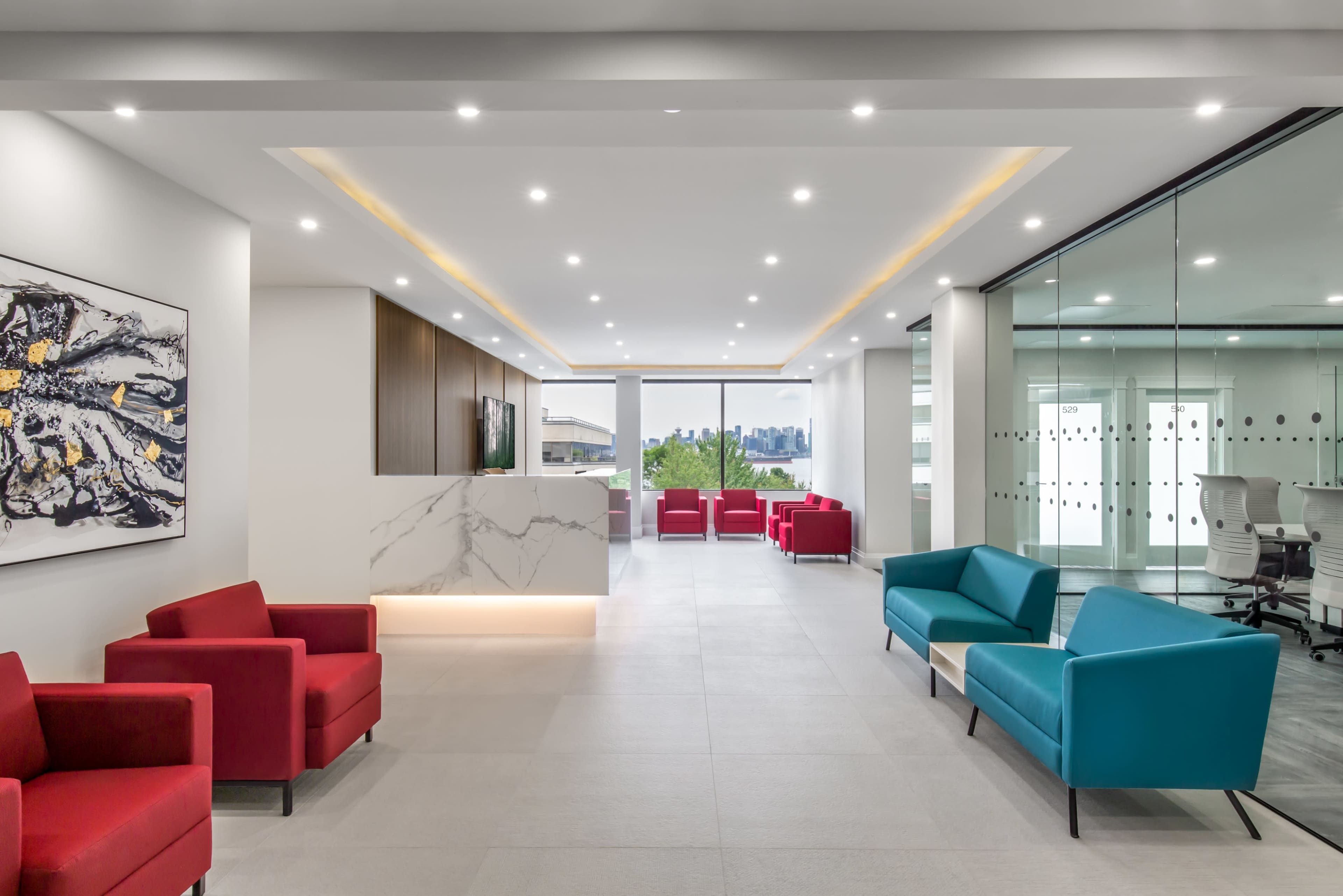 A modern office reception area featuring red and blue seating, a marble reception desk, and large windows overlooking a city skyline.