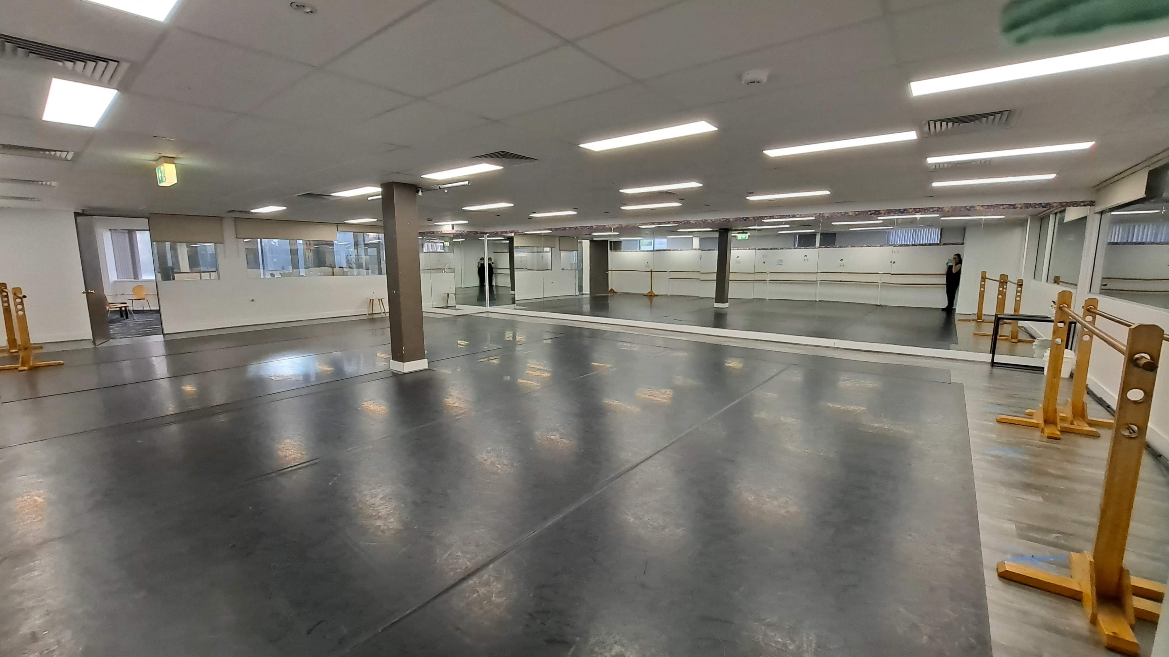 A large, empty dance studio with mirrors along two walls and wooden ballet barres positioned on both sides.