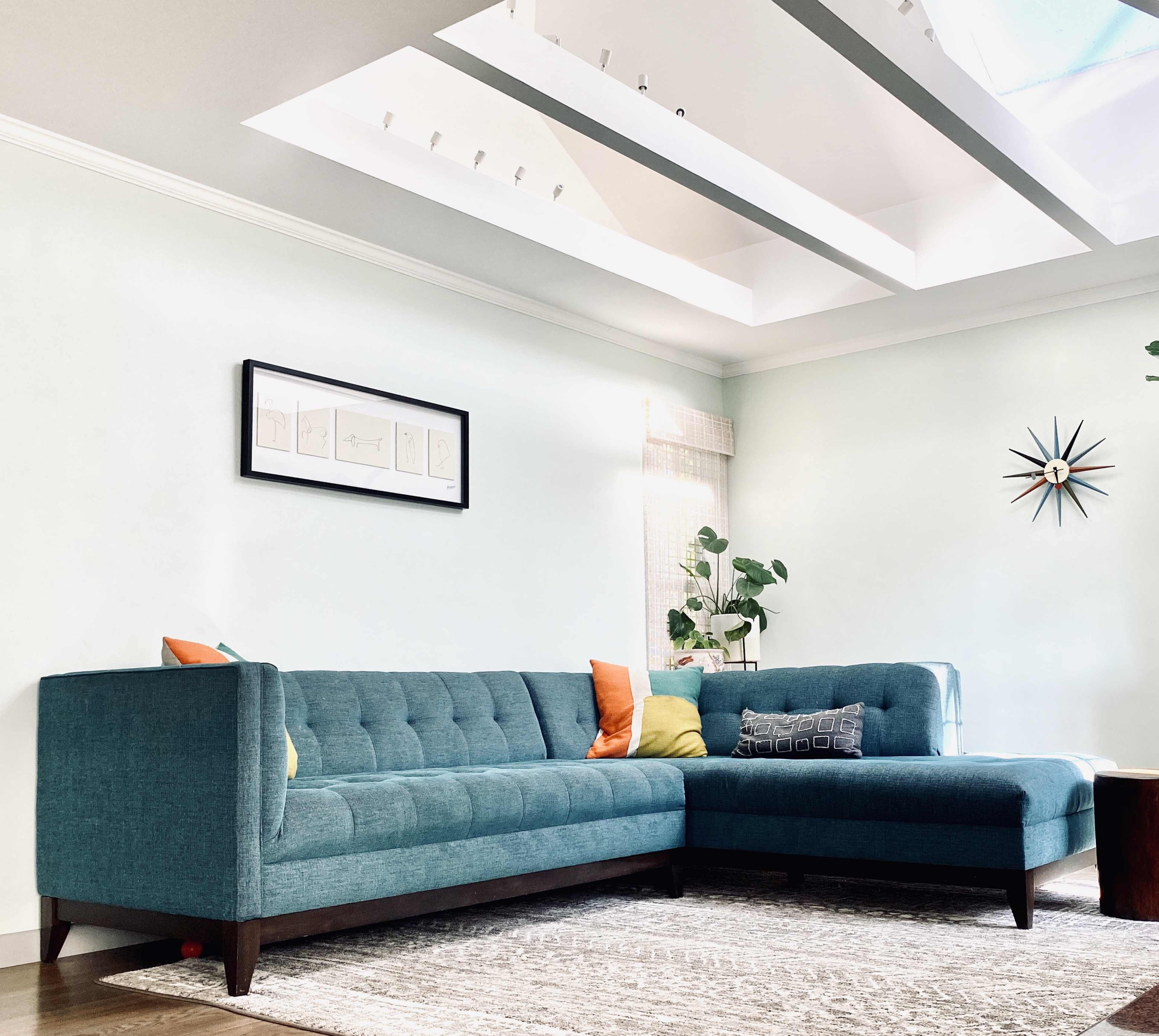 A modern living room featuring a teal sectional sofa, a patterned rug, and a skylight above.