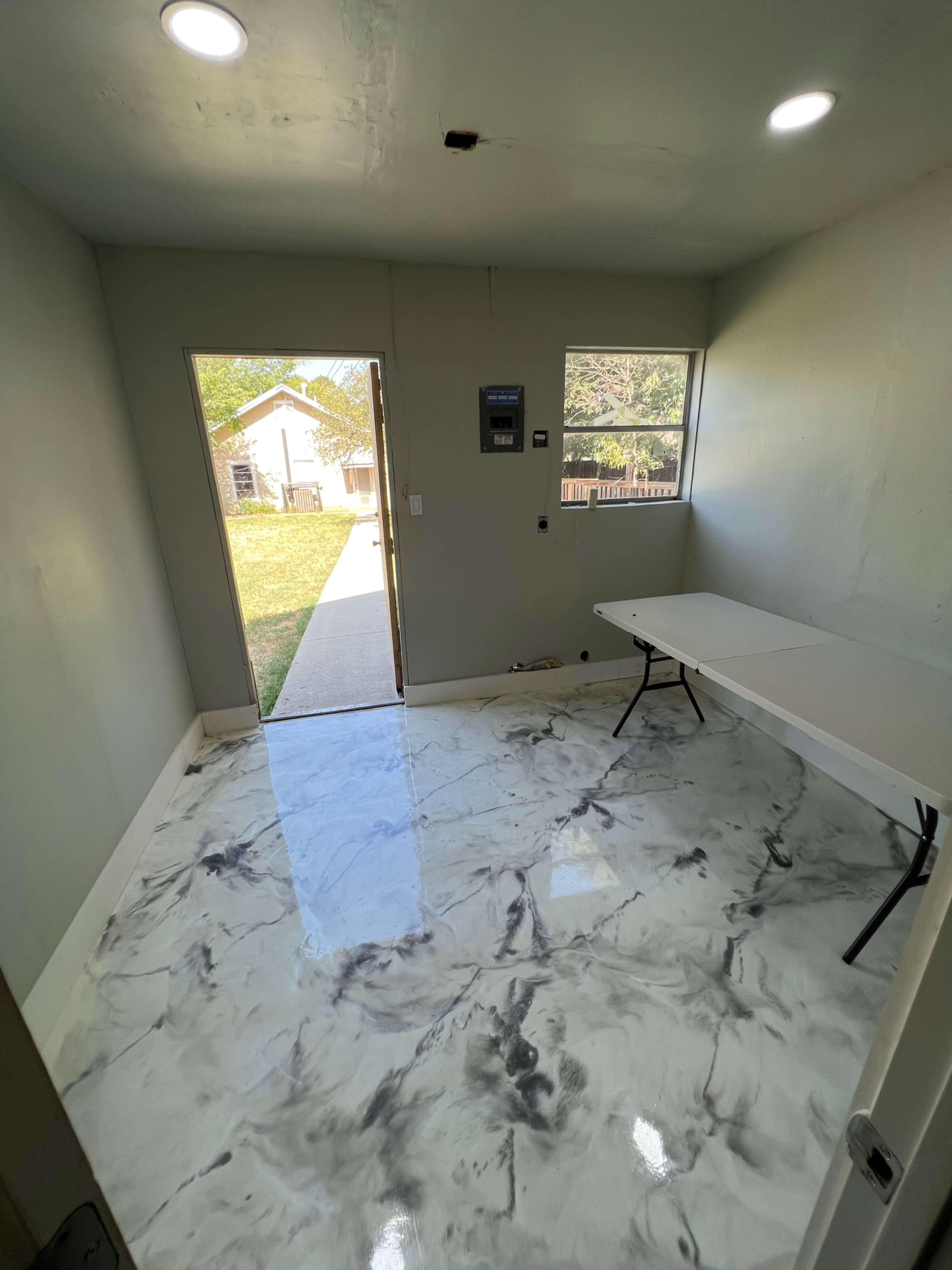 A sparsely furnished room with a marble-patterned floor, a single table, and a doorway leading outside.