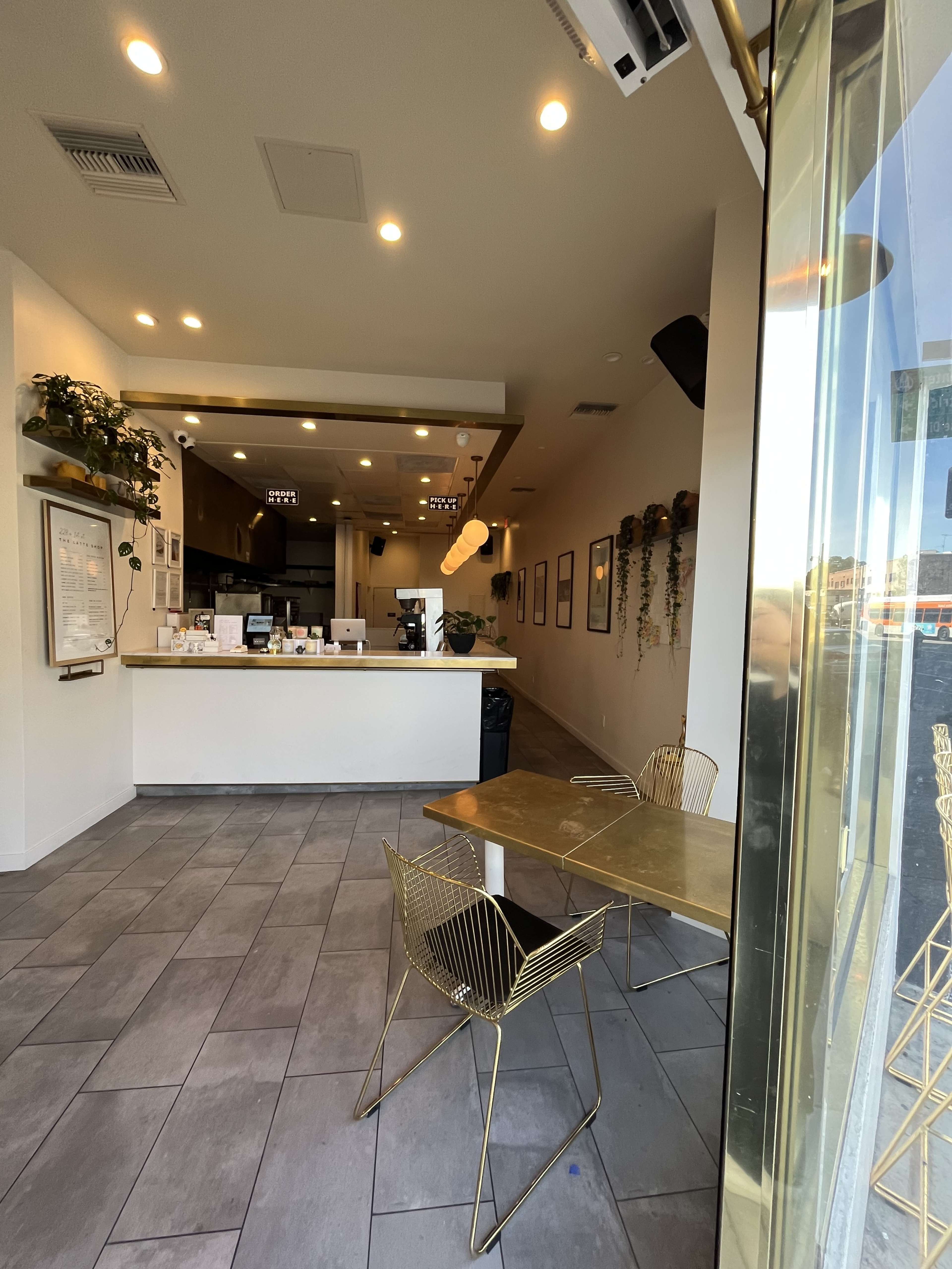 A modern café interior with a reception counter, tables, and decorative plants.