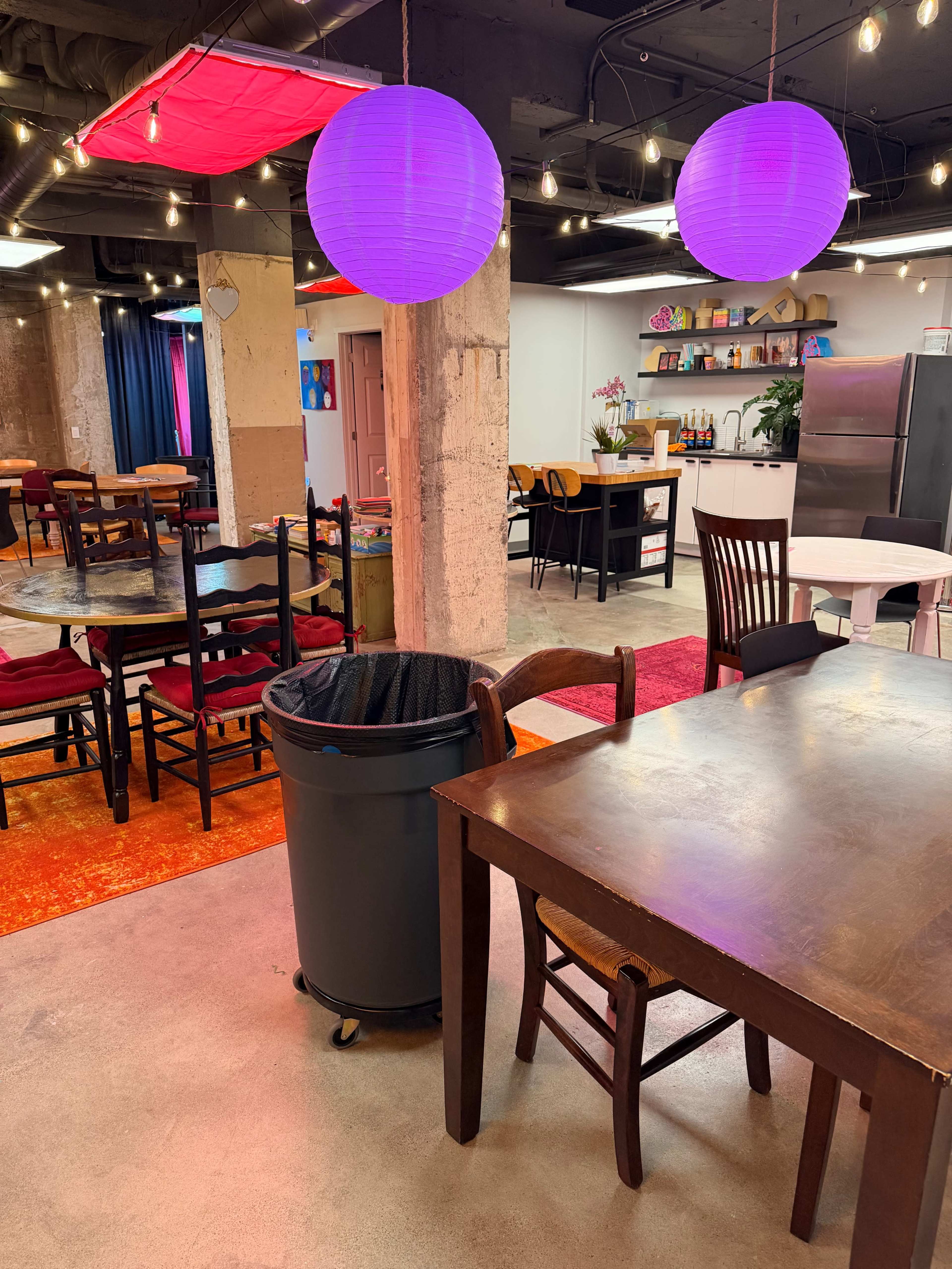 The image shows a colorful dining area with circular purple lights hanging from the ceiling, tables with chairs, and a trash can in the foreground.