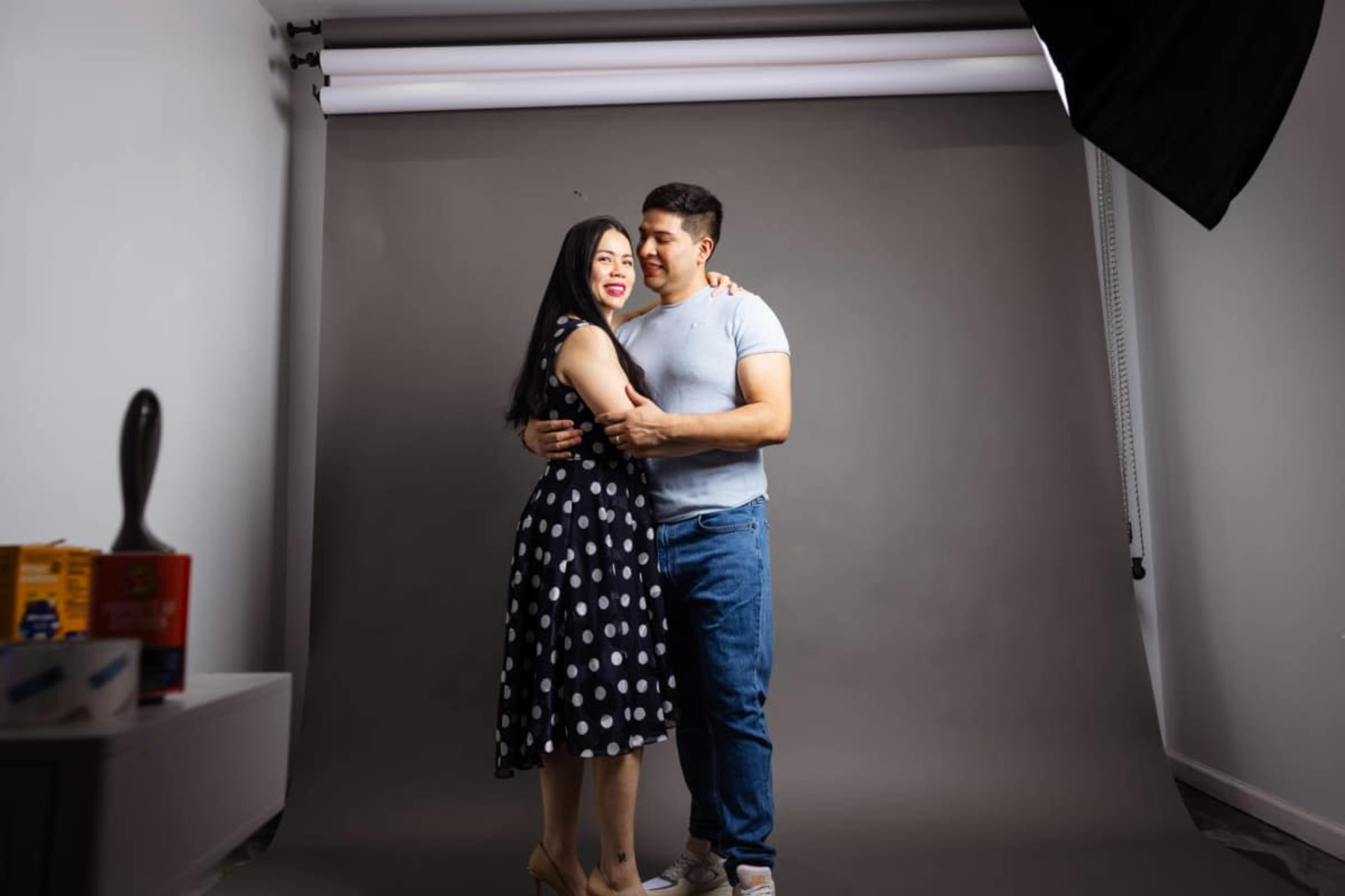 A couple stands closely together in a studio setting with a neutral gray backdrop.
