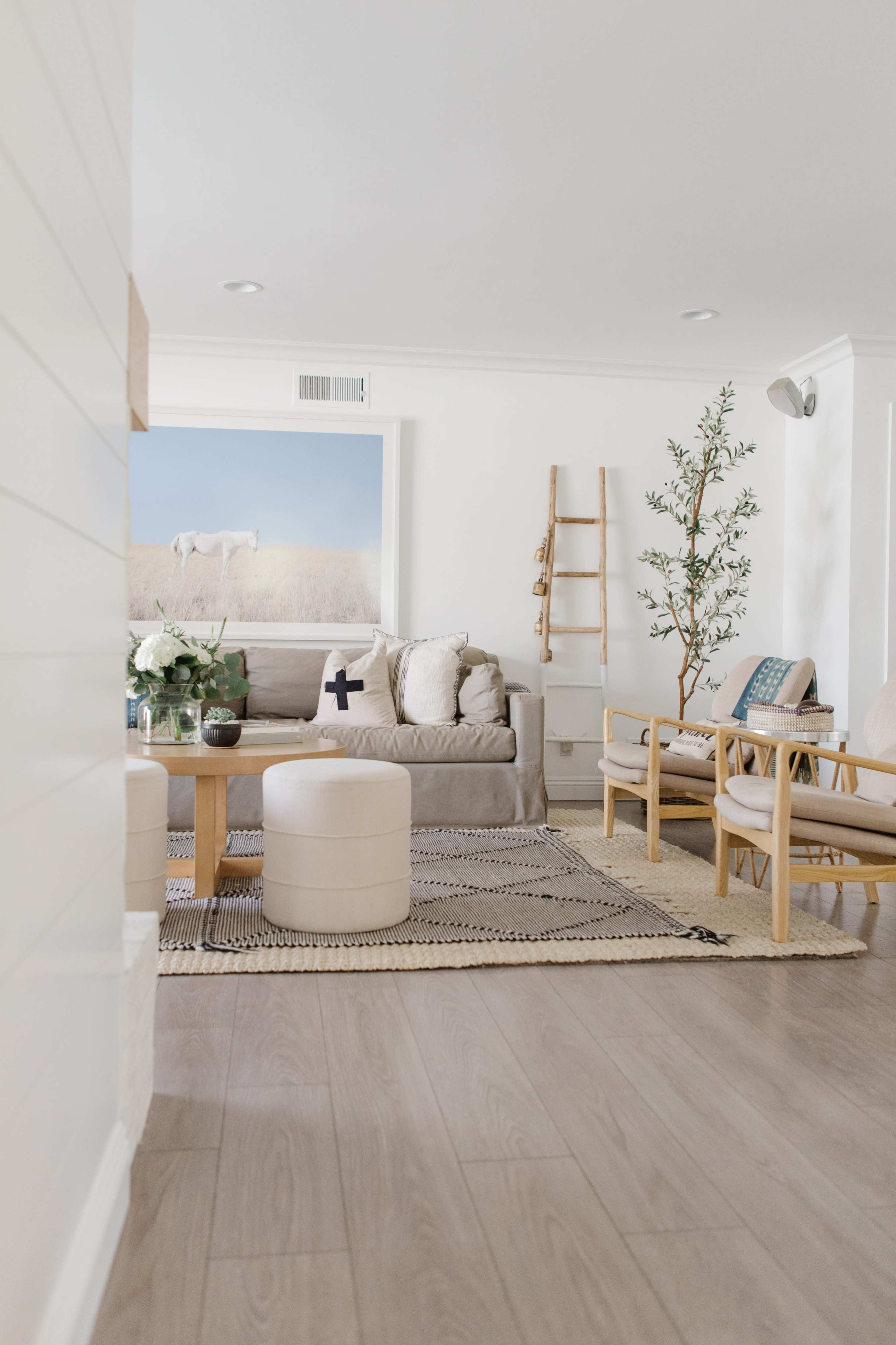 A light and airy living room with a beige couch, wooden furniture, and a decorative ladder against the wall.