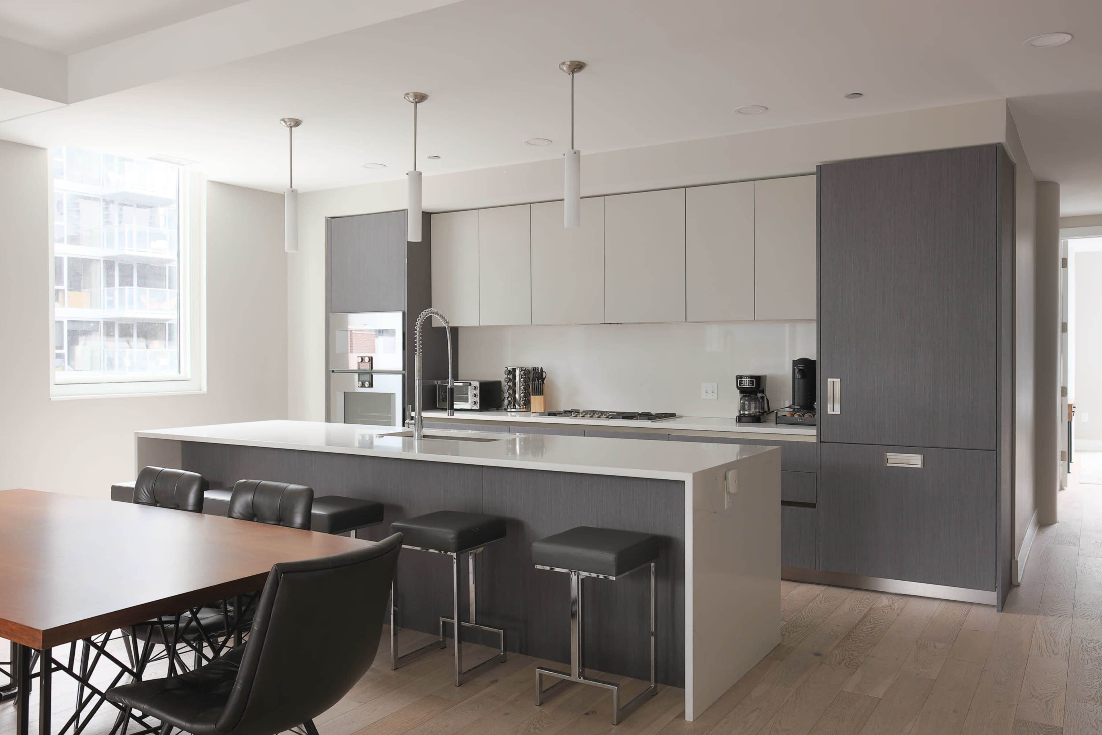 A modern kitchen with a central island, sleek cabinetry, and a dining area featuring a wooden table and black chairs.