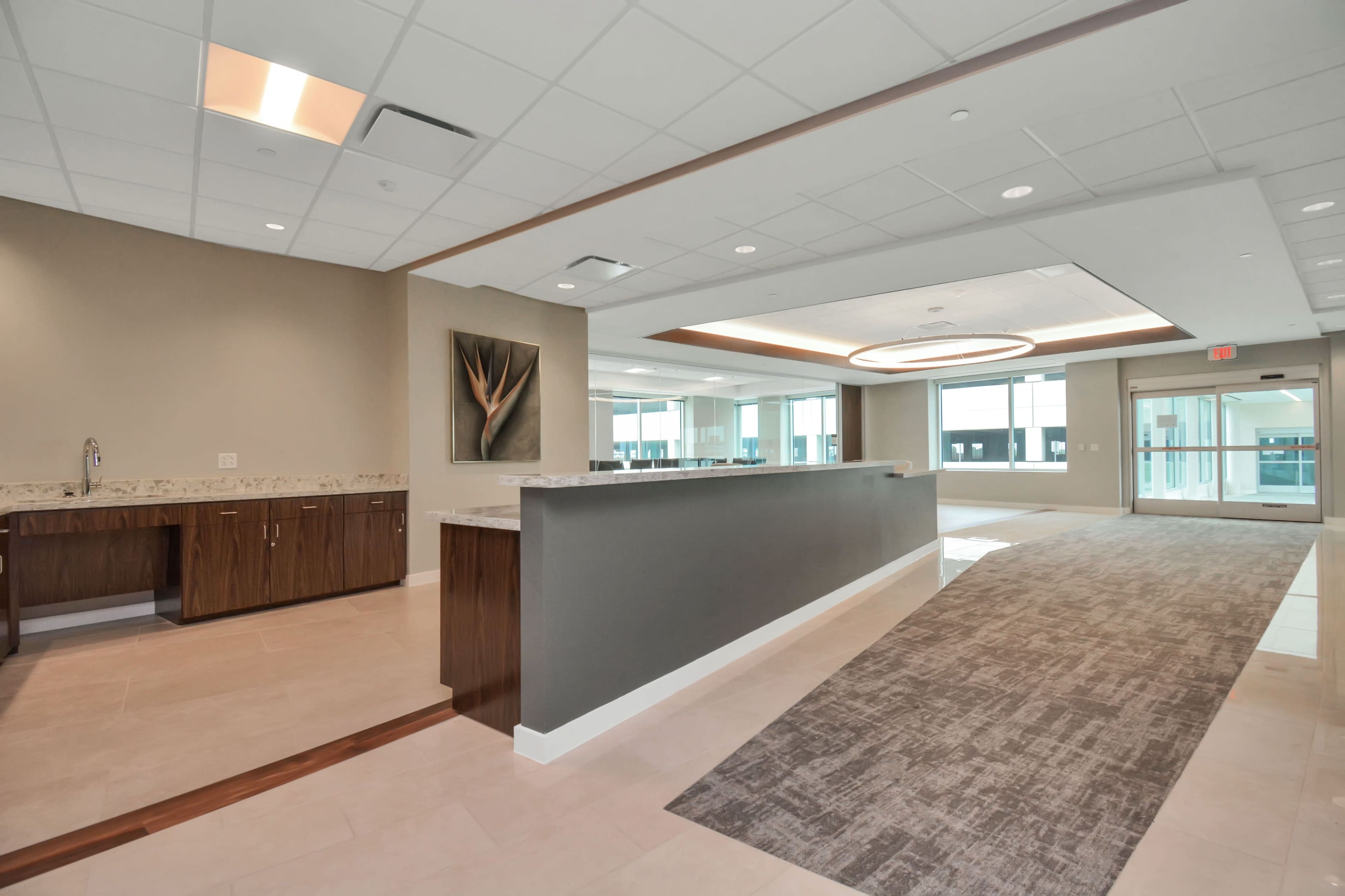 A modern office reception area with a long counter, beige walls, and large windows allowing natural light.