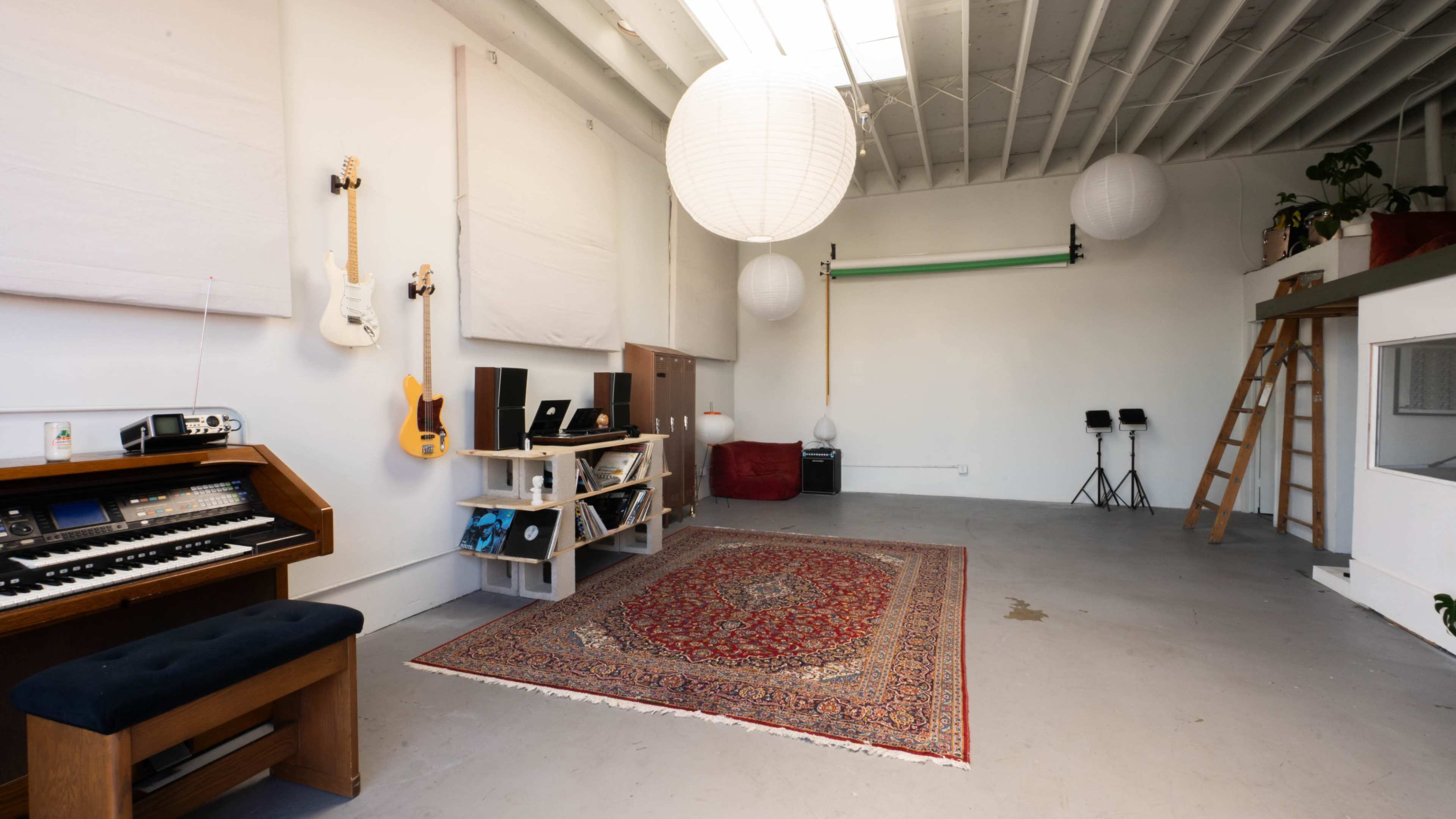 A spacious music studio with a wooden keyboard, a patterned rug, and various lighting fixtures hanging from the ceiling.