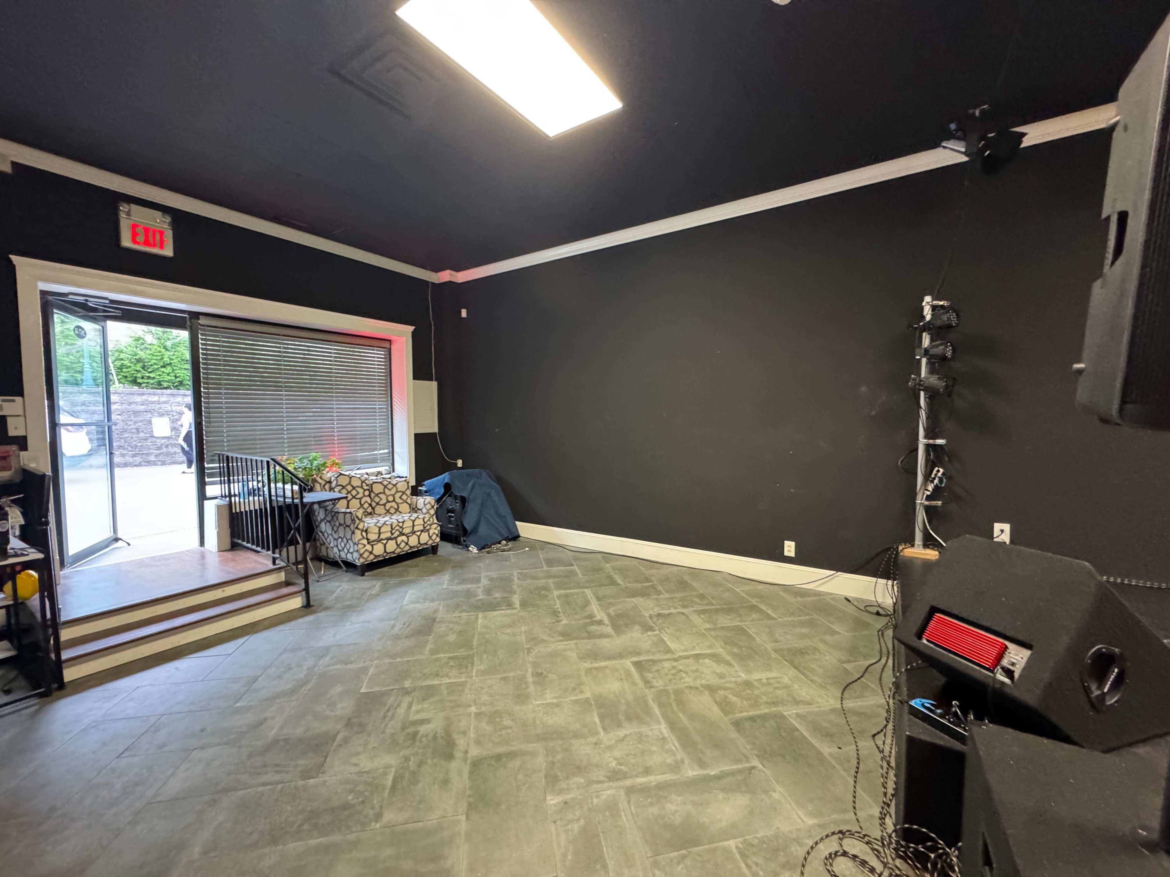 The image shows an empty room with black walls, a tiled floor, a couch in the corner, and a small staircase leading to an exit.