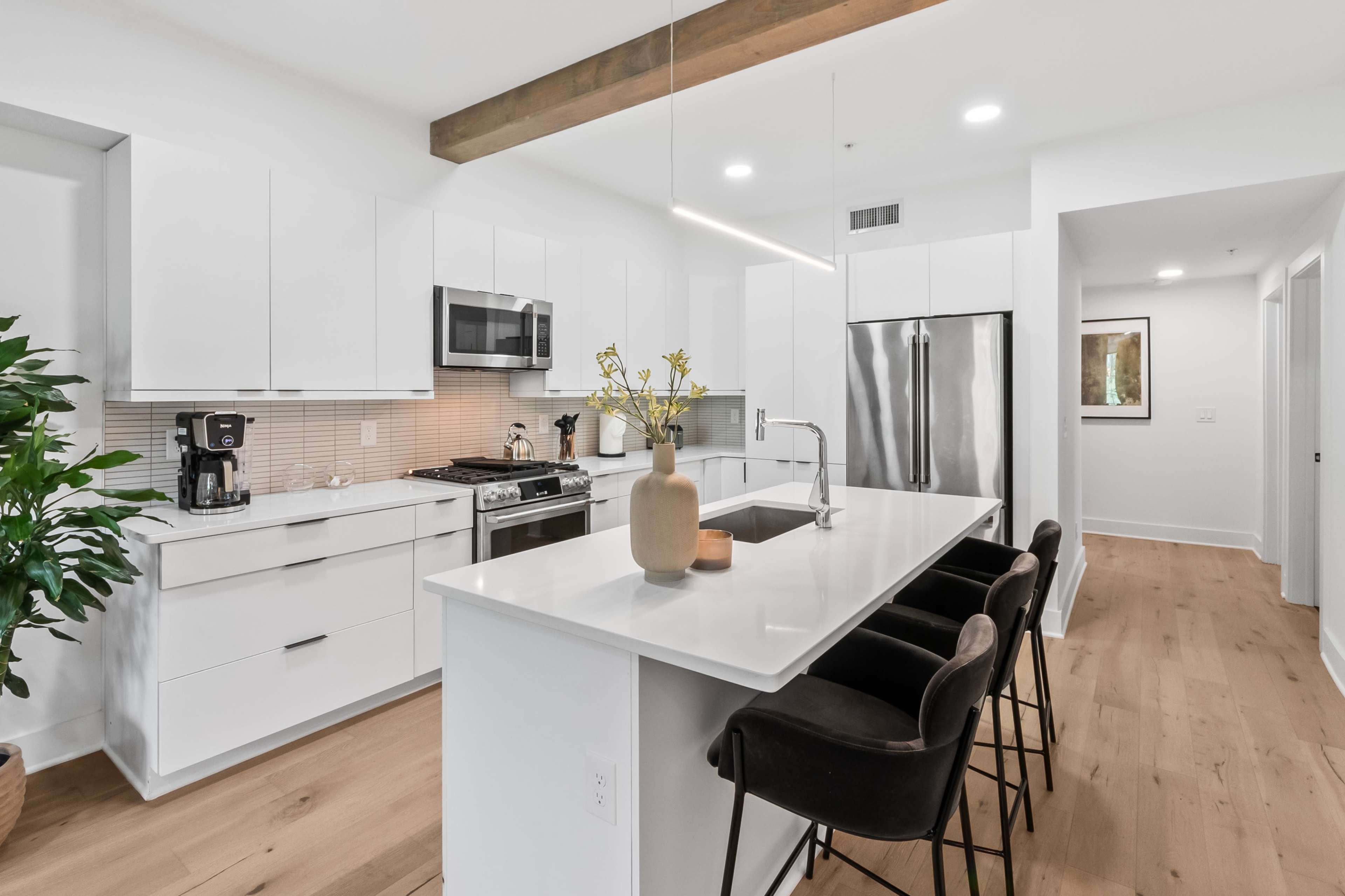 The image shows a modern kitchen featuring white cabinetry, stainless steel appliances, and a central island with bar seating.