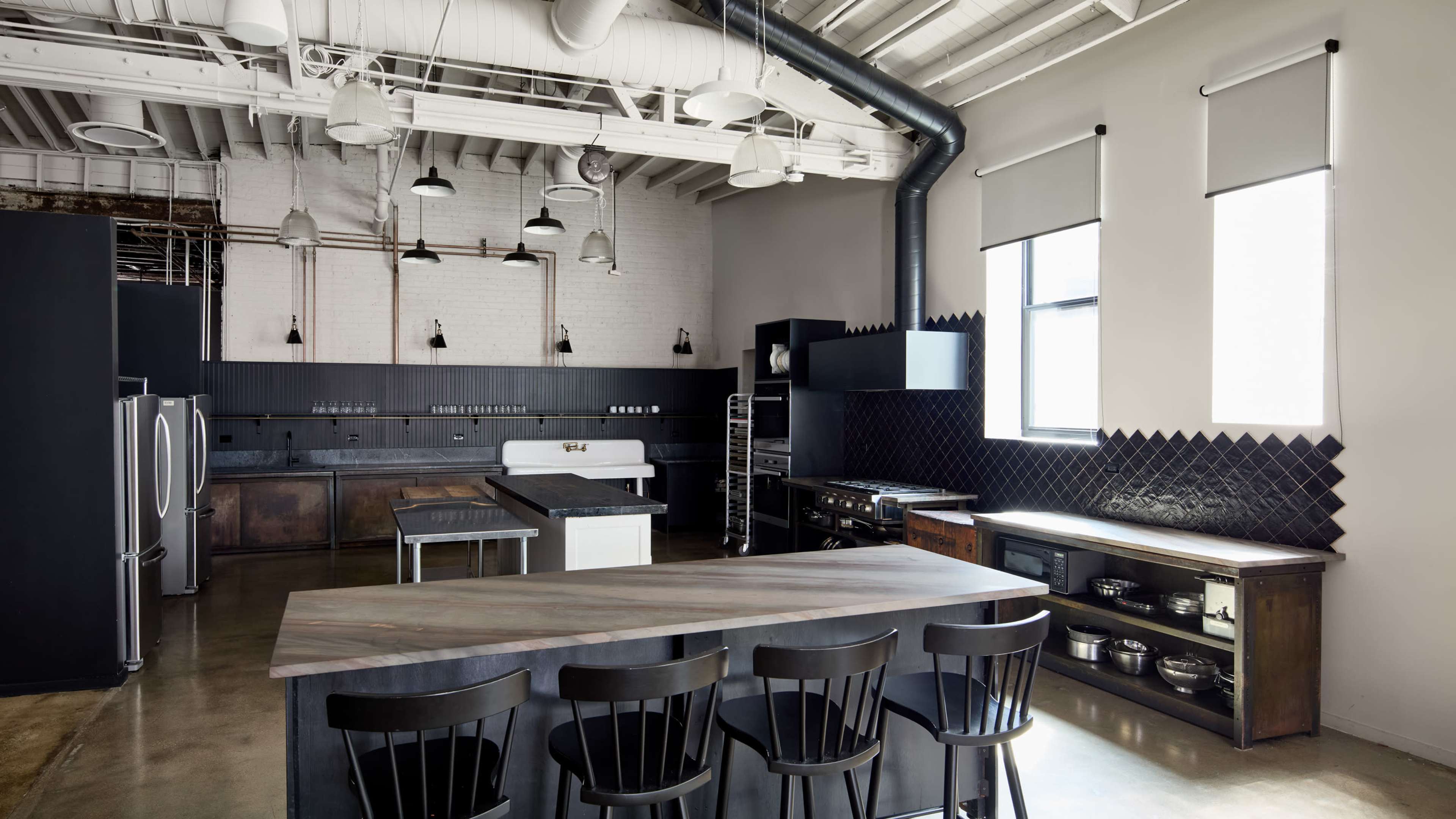 The image shows a modern kitchen with a large island, black cabinetry, and overhead pendant lighting.