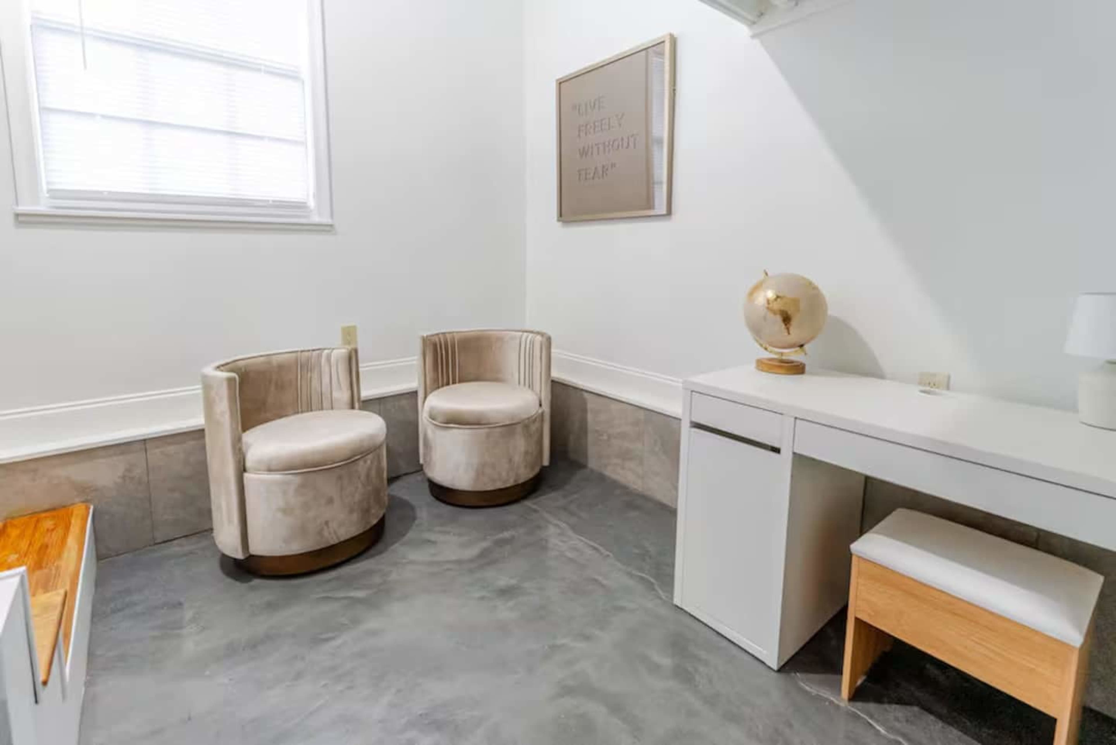 The image shows a small room with two beige upholstered chairs, a white desk, and a decorative globe, all set against a light-colored wall.