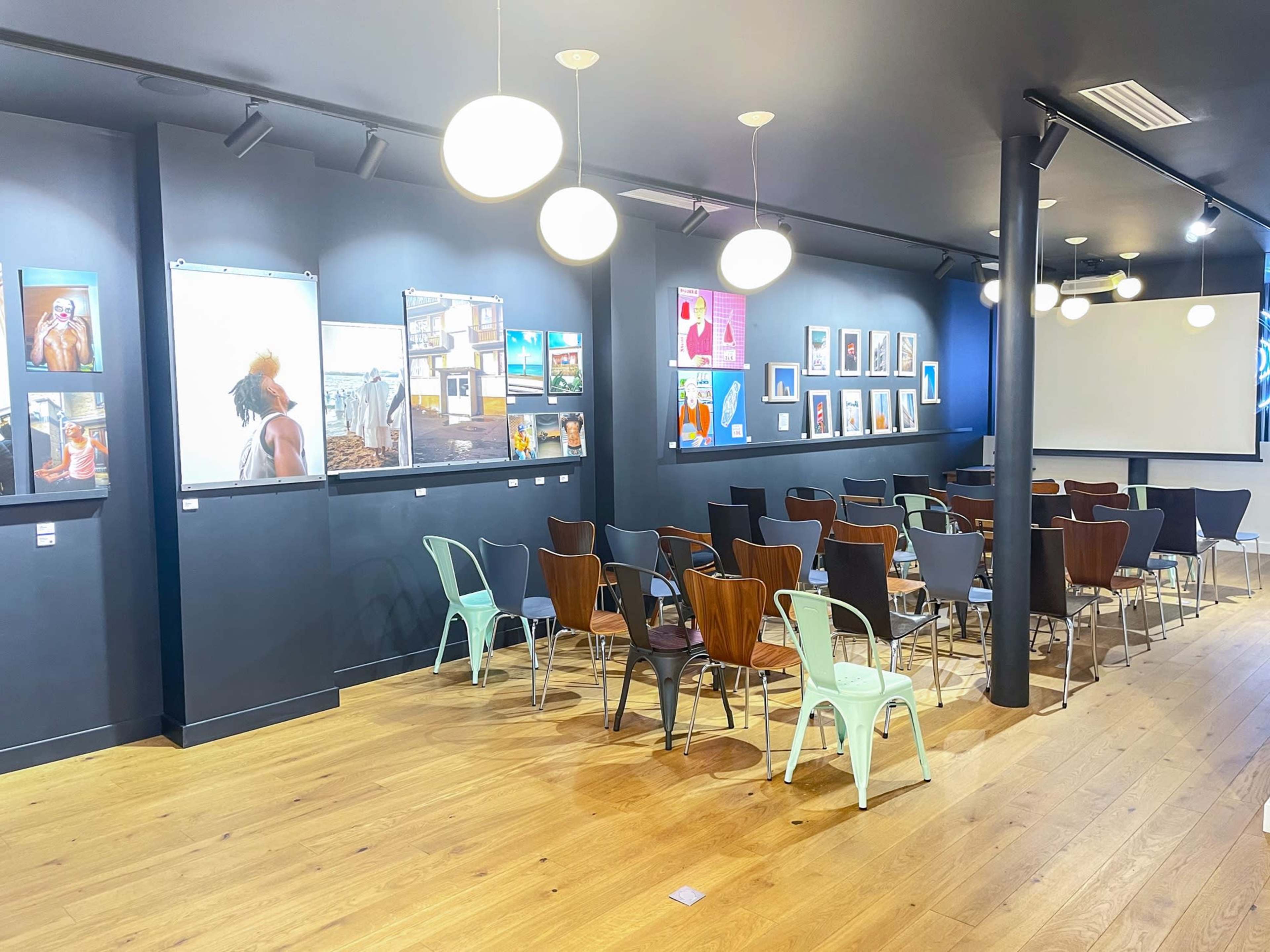 The image shows a modern event space with a wall art display and rows of chairs arranged in a semi-circle facing a screen.