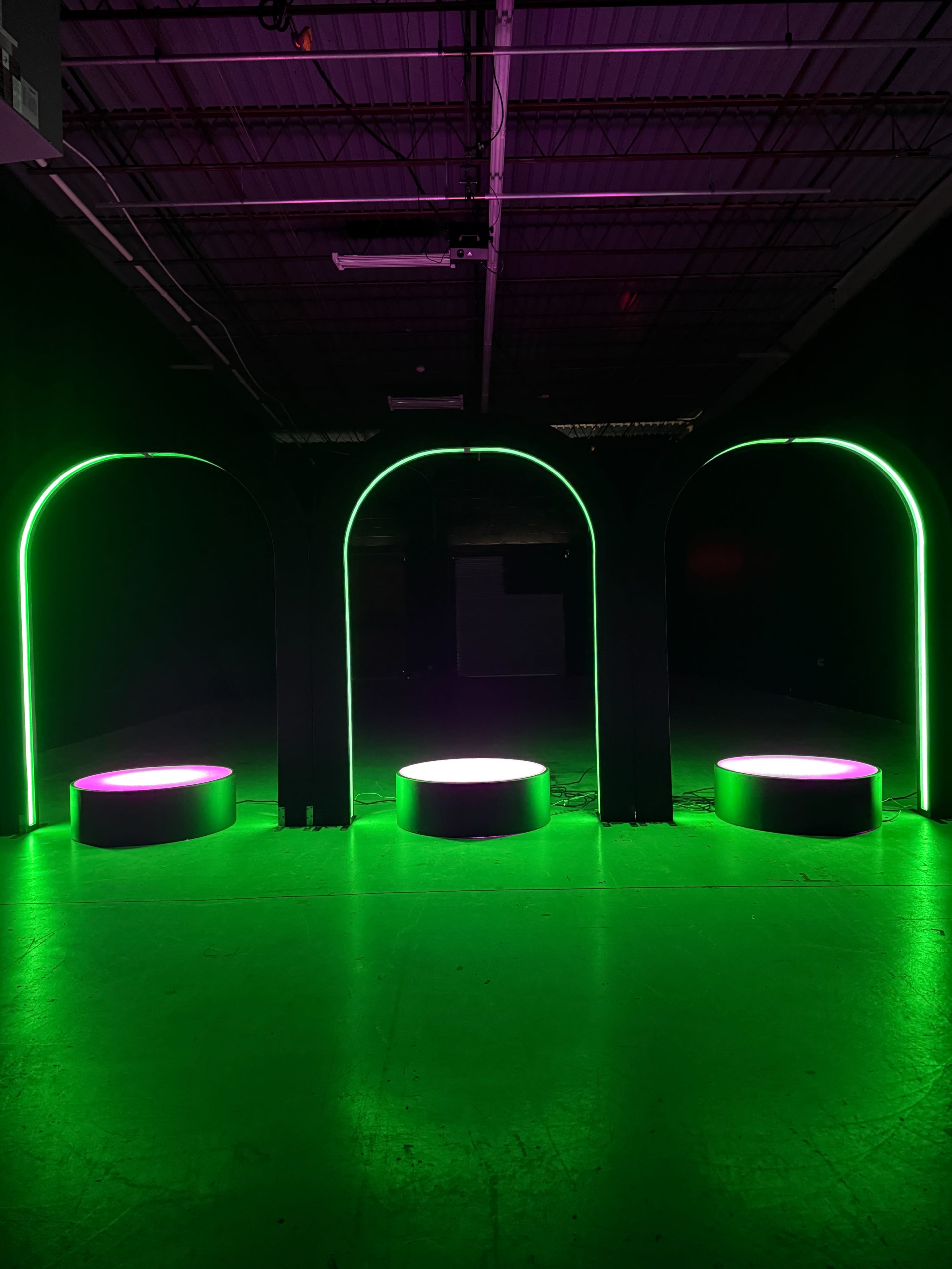 The image shows three circular platforms illuminated by green and pink lights, set against a dark background with arching structures.