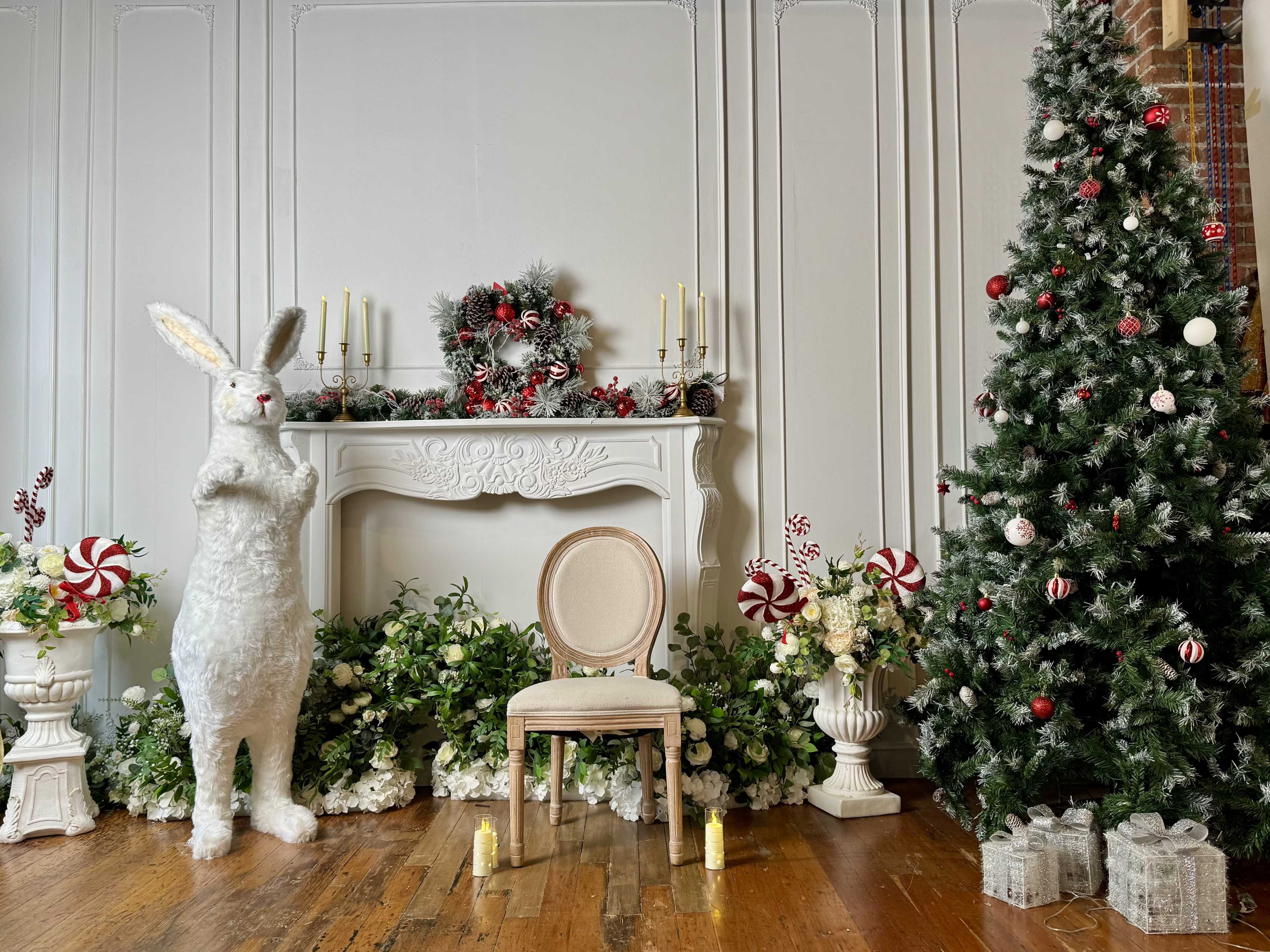 A large white rabbit statue stands beside a decorated Christmas tree and a mantel adorned with festive decorations, while a single chair is placed in front of the scene.