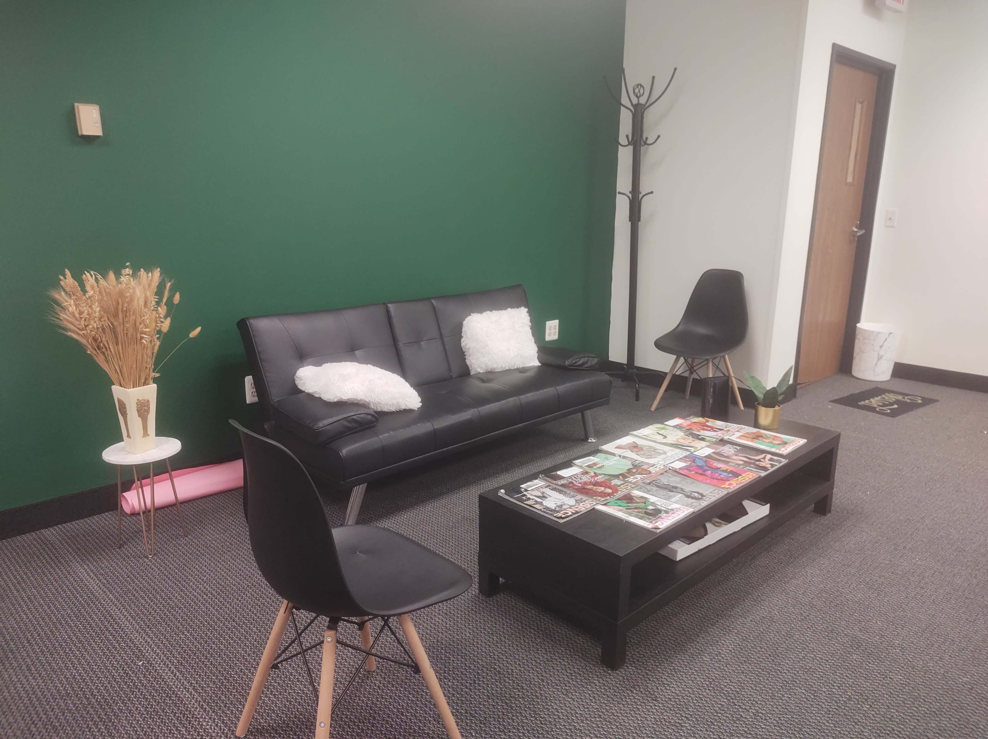 A minimalist living space with a black sofa, a coffee table covered in magazines, and a green accent wall.