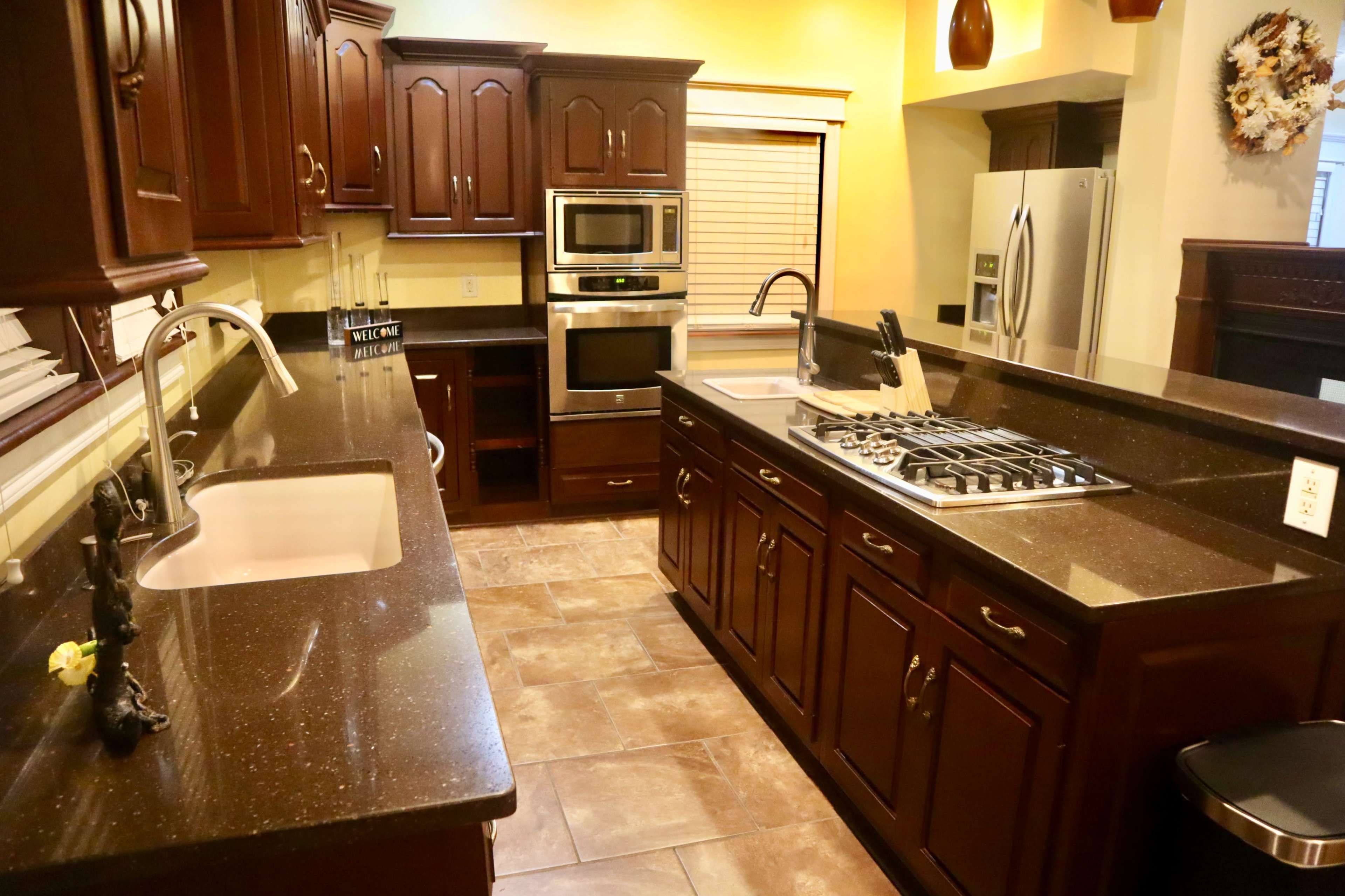 A modern kitchen features dark wooden cabinets, stainless steel appliances, and a large countertop with a gas stove and sink.