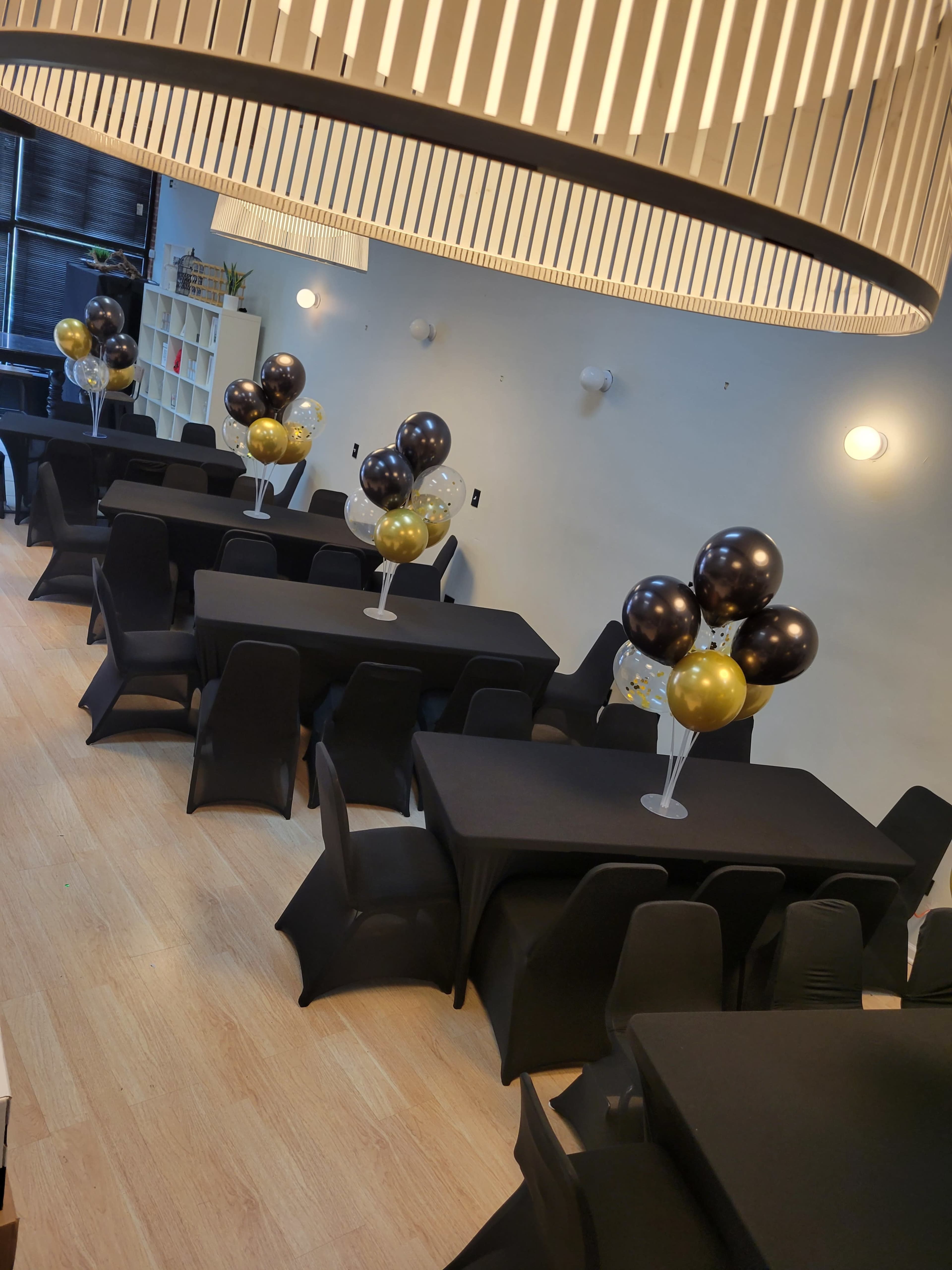 A well-arranged event space featuring multiple black tables, each adorned with balloon centerpieces in black, gold, and white.